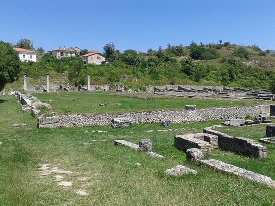 Siti Archeologici in Abruzzo: Alba Fucens - Avezzano (Aq) Alba Fucens, situata nei pressi di Avezzano in provincia dell'Aquila, è uno dei siti archeologici più importanti d'Abruzzo. Fondata dai Romani nel 304 a.C. come colonia di diritto latino, la città occupava una posizione strategica ai piedi del Monte Velino, a quasi 1.000 metri di altitudine. Il toponimo "Alba" deriva dalla radice indoeuropea con il doppio significato di "altura" e "bianco", probabilmente in riferimento ai sassi bianchi della zona. Il termine "Fucens" si ricollega invece al vicino Lago Fucino, associato all'etnico Fūcentes, nome con cui erano conosciuti i Marsi che abitavano le sponde del lago. La città si sviluppò rapidamente grazie alla sua posizione lungo la via Tiburtina Valeria, importante arteria di collegamento. I primi 6.000 coloni costruirono una solida cinta muraria per difendersi dagli attacchi degli Equi, che tentarono senza successo di espugnarla. Alba Fucens divenne un baluardo militare fondamentale per il controllo dei territori circostanti e mantenne un ruolo strategico durante tutta l'epoca romana. Gli scavi archeologici sistematici, iniziati nel 1949 dall'Università di Lovanio e proseguiti dal Centro belga di ricerche archeologiche in Italia, hanno riportato alla luce gran parte della struttura urbana. La città era racchiusa da una cinta muraria lunga circa 2,9 km, costruita con grandi massi poligonali incastonati perfettamente. Particolarmente interessante è la triplice linea difensiva sul lato settentrionale, a testimonianza dell'importanza della sicurezza nella città. Ancora visibili sono le porte, i bastioni e i simboli apotropaici scolpiti sulle mura. Il cuore di Alba Fucens era il forum, circondato dagli edifici pubblici più importanti come la basilica, il macellum e le terme, impreziosite da mosaici con scene marine. L'anfiteatro, situato ai margini della città, rappresentava uno dei luoghi di intrattenimento principali. Tra le residenze patrizie spicca la Domus, attribuita ipoteticamente a Quinto Nevio Sutorio Macrone. Sulla collina occidentale sorgeva il Tempio di Apollo. Amiternum fu fondata dal popolo dei Sabini e fu una delle loro città principali, almeno fino alla conquista romana. L’antica città di Amiternum si trova sul colle di San Vittorino, tra Coppito e Pizzoli ed essendo collocata tra importanti strade come la via Salaria, la via Cecilia e la via Claudia Nova, divenne un punto di riferimento per tutta l’area circostante arricchendosi di strutture architettoniche importanti. L’area archeologica conserva diversi resti romani, soprattutto luoghi dedicati allo svago pubblico. Di età augustea sono sia il teatro che l’anfiteatro, entrambi ben visibili e in un buono stato di conservazione. Il primo, risalente al I secolo a.C., poteva ospitare 2000 spettatori. Si possono vedere ancora con chiarezza l’orchestra, la scena e i rivestimenti murari in opus reticolatum. L’anfiteatro, invece, è una struttura del I sec d.C., pensata e realizzata per una capienza di 6000 spettatori. Della struttura è visibile solo il primo livello di forma circolare, con il perimetro tracciato da 48 grandi arcate. Alcuni elementi decorativi e architettonici, ad esempio i fregi e alcune colonne del teatro, sono conservati al Museo Nazionale d’Abruzzo (MUNDA) a L’Aquila.
