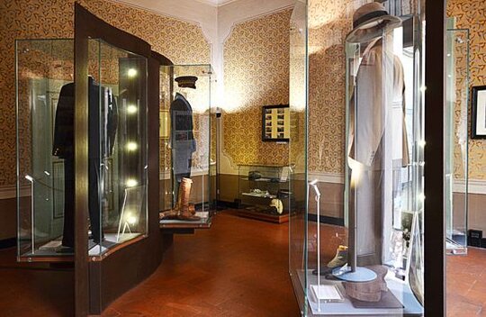Nel cuore del centro storico di Pescara, lungo l’antico corso principale, sorge la casa natale di Gabriele d’Annunzio. Questa dimora, costruita all’interno della fortezza militare che un tempo delimitava la città, fu dichiarata Monumento Nazionale nel 1927, grazie alla volontà dello stesso Poeta e al decreto di Mussolini. Passata al Demanio nel 1958, è oggi gestita dal Ministero per i Beni e le Attività Culturali. Nonostante i diversi interventi di restauro, l’edificio ha conservato la sua struttura originale di casa borghese ottocentesca. Al piano terra si apre un piccolo cortile interno, raccolto e silenzioso, con un caratteristico pozzetto in laterizio. Gabriele d’Annunzio nacque in questa casa il 12 marzo 1863 e vi trascorse l’infanzia fino all’età di undici anni, quando lasciò Pescara per studiare a Prato. Rientrò più volte in Abruzzo per far visita alla madre, rimasta nella dimora di famiglia, lasciandosi alle spalle il ricordo dolce e malinconico di un’infanzia serena. Il percorso museale, al primo piano dell’edificio, si sviluppa attraverso cinque stanze che conservano l’atmosfera dell’epoca, con arredi originali, dipinti e oggetti quotidiani. Ogni ambiente restituisce al visitatore il senso profondo di una casa vissuta, un luogo intimo che racconta i primi anni del Poeta. A guidare l’esperienza è proprio la voce di d’Annunzio, attraverso citazioni tratte dal Notturno, riportate su pannelli all’interno delle stanze. Questi brani evocano emozioni, ricordi familiari e il legame profondo con la casa natale. Le stanze di rappresentanza, splendidamente affrescate a metà Ottocento da artisti marchigiani, sono arricchite da decorazioni a tempera che propongono motivi neoclassici con figure mitologiche, elementi vegetali e animali fantastici. Si tratta della più antica testimonianza pittorica della città, giunta fino a noi intatta nella sua eleganza. La visita prosegue con l’esposizione dedicata al guardaroba del Poeta, figura centrale della cultura e della moda del suo tempo. Vi si trovano capi iconici come il cappotto rosso per la caccia e i sandali dorati indossati durante l’estate. Le sale successive ospitano le prime edizioni delle sue opere, impreziosite da xilografie, e i calchi del volto e della mano eseguiti la notte della sua morte nel 1938 dallo scultore Arrigo Minerbi. Una stanza è interamente dedicata alla sua figura di soldato, con cimeli, uniformi, fotografie e pannelli che illustrano le sue imprese militari. A completare il percorso, al piano terra, è visitabile l’antica stalla, che ricorda il profondo affetto di d’Annunzio per i suoi primi cavalli, Aquilino e Murgione, detto Silvano.
