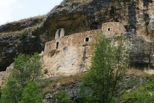 I luoghi sacri in Abruzzo: Tra le rocce del monte Velino verso l’Eremo di San Benedetto. Tra le rocce del monte Velino verso l’Eremo di San Benedetto. Il Monte Velino, con la sua imponenza e il suo carattere selvaggio, è da secoli un luogo di profonda spiritualità. Questa montagna, la terza più alta dell’Appennino, domina il paesaggio abruzzese con i suoi pendii scoscesi e le sue valli silenziose, offrendo rifugio a chi cerca solitudine e raccoglimento. Il contrasto tra il versante boscoso che si affaccia sull’Altopiano delle Rocche e quello ripido che precipita verso la piana del Fucino crea un ambiente aspro e suggestivo, perfetto per chi desidera avvicinarsi al divino attraverso la contemplazione della natura. Da secoli, il Velino è stato meta di eremiti e pellegrini alla ricerca di un luogo in cui il sacro si manifestasse nella sua essenza più pura. Seguendo antichi sentieri che attraversano il fianco della montagna, si giunge a un luogo simbolo della spiritualità abruzzese: l’Eremo di San Benedetto. Questa grotta, incastonata a 1.610 metri di altitudine in una parete rocciosa, è stata per secoli dimora di monaci e asceti, che qui trovavano il silenzio necessario alla meditazione e alla preghiera. Il legame con San Benedetto richiama la tradizione monastica, basata sulla rinuncia e sulla ricerca interiore, principi che hanno guidato la vita di coloro che hanno abitato questi luoghi impervi. Dalla grotta, lo sguardo si apre sulla vastità del Fucino e sulle cime dei Monti Simbruini, creando un senso di connessione profonda tra l’uomo e l’infinito. Questo panorama mozzafiato diventa esso stesso parte del cammino spirituale, un invito a distaccarsi dal mondo terreno e a elevarsi verso qualcosa di più grande. L’eremo, scolpito nella pietra e immerso nel silenzio, racconta di una fede che ha resistito nei secoli, alimentata dalla forza della natura e dall’isolamento che rende questi luoghi così carichi di misticismo. Ancora oggi, l’Eremo di San Benedetto continua a essere un punto di riferimento per escursionisti e fedeli che cercano un’esperienza fuori dal tempo. Il sentiero che conduce alla grotta, tra boschi e pareti rocciose, sembra ripercorrere antiche vie di fede, dove il cammino fisico si intreccia con quello interiore. Qui, tra le rocce del Monte Velino, il culto si esprime nella sua forma più essenziale, lontano dai rumori della civiltà, in un dialogo silenzioso tra l’uomo, la montagna e il divino.