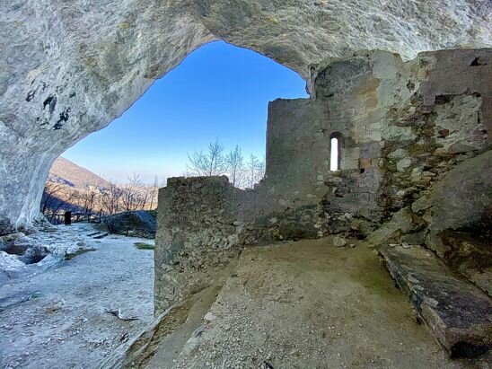 La Grotta di Sant’Angelo, incastonata nel suggestivo borgo di Palombaro, è un luogo che custodisce secoli di storia e spiritualità. Raggiungibile con una breve escursione di circa 15 minuti dall’area pic-nic sottostante, la grotta si presenta come una cavità naturale avvolta dalla rigogliosa vegetazione del Parco Nazionale della Majella. Al suo interno si trovano i resti di una chiesa rupestre dedicata a San Michele Arcangelo, costruita tra l’XI e il XII secolo sopra uno sperone di roccia, un tempo consacrato alla dea Bona, divinità della fertilità. Le vasche scavate nella roccia, ancora visibili, servivano per la raccolta di acqua piovana, utilizzata in antichità per rituali legati alla fertilità. Secondo la tradizione, le puerpere si recavano presso la grotta per cospargersi il seno con l’acqua delle sorgenti, invocando abbondanza di latte. Questo rito, tramandato nei secoli, testimonia l’importanza del luogo come punto di riferimento spirituale e antropologico. Recenti scavi archeologici, condotti dal Dipartimento di Archeologia dell’Università G. D’Annunzio di Chieti su concessione del MIBAC, hanno permesso di approfondire la conoscenza delle origini storiche del sito. Le ricerche hanno portato alla luce reperti e strutture che confermano la continuità del culto, dalla preistoria fino al medioevo, arricchendo il patrimonio culturale della zona. La visita alla Grotta di Sant’Angelo offre un’esperienza immersiva tra natura, storia e spiritualità. Il sentiero che conduce alla grotta si snoda attraverso boschi di faggi e radure, creando un percorso affascinante che invita alla contemplazione e al contatto con la natura. Un luogo di pace e mistero, capace di raccontare le profonde radici del territorio abruzzese.