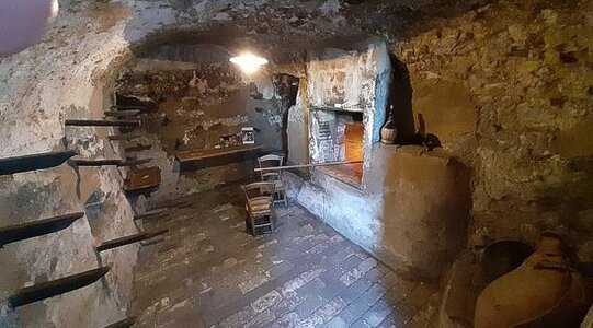 Il Museo Civico Etnografico di Castel del Monte, situato in uno dei borghi più suggestivi delle montagne aquilane, rappresenta un’importante testimonianza della vita tradizionale di questa comunità. Il museo si distingue per la sua particolare concezione di "museo diffuso", che non si limita a uno spazio chiuso, ma si sviluppa lungo le vie del borgo, integrandosi con gli edifici storici e raccontando la storia di un popolo che ha vissuto in simbiosi con la montagna e la pastorizia. All'interno di vecchi locali recuperati, sono stati ricreati ambienti che riproducono la vita quotidiana dei pastori, mostrando oggetti e strumenti utilizzati nelle attività tradizionali. Ogni angolo del museo è pensato per evocare l’antica vita pastorale di Castel del Monte, un paese conosciuto anche come "la Capitale dei Pastori" per la sua secolare tradizione legata all’allevamento e alla transumanza. La pastorizia è stata, infatti, per secoli l'attività principale della comunità castellana, e il museo rende omaggio a questo aspetto fondamentale della cultura locale. Le ricostruzioni di ambienti come il mulino, il forno del ballo e la casa antica, insieme agli strumenti legati all'arte della lana, permettono di immergersi completamente in un passato che ha modellato il presente di Castel del Monte. Castel del Monte ha avuto un ruolo significativo nella storia del cinema, diventando una meta ambita da registi di fama internazionale. Il borgo è stato scelto come set per importanti film, tra cui "The American", con George Clooney e Violante Placido. Il paesaggio mozzafiato e l’autenticità degli ambienti hanno fatto di Castel del Monte un luogo ideale per raccontare storie di mistero e riflessione, conferendo al museo e al borgo un’aura ancora più affascinante e suggestiva. La combinazione di bellezza naturale e tradizione culturale ha reso il paese un punto di riferimento anche per il mondo del cinema. Una visita al Museo Civico Etnografico di Castel del Monte è un’esperienza che va oltre la semplice scoperta di oggetti storici. È un viaggio nel tempo che consente di entrare in contatto con la storia di una comunità forte e resiliente, che ha saputo preservare le proprie tradizioni nonostante le difficoltà. Grazie alle visite guidate organizzate dalla cooperativa InCastello, i visitatori hanno l’opportunità di scoprire, passo dopo passo, come la pastorizia e le tradizioni locali siano ancora vive nel cuore del borgo, portando alla luce la storia di un popolo che ha saputo trasformare il sacrificio quotidiano in una risorsa per la propria identità.