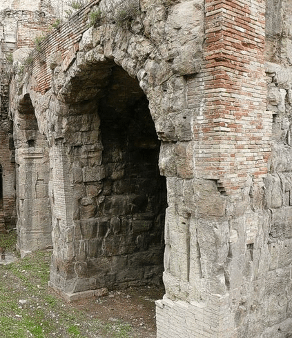 Il Teatro Romano di Teramo, situato nel centro storico della città, rappresenta uno dei più importanti e ben conservati esempi di architettura romana in Abruzzo. L'edificio si trova tra via Teatro Antico e via Luigi Paris, nelle vicinanze del Duomo e a pochi passi dall'Anfiteatro romano. Il teatro fu costruito nell'antica città di Interamnia, oggi Teramo, che si sviluppava lungo il fiume Tordino. Questo sito archeologico è un punto di riferimento fondamentale per comprendere la vita culturale e sociale della città durante l'epoca romana, testimoniando l'importanza che il teatro aveva come luogo di incontro e di spettacolo per i cittadini. Il teatro fu edificato in età augustea, attorno al 30 a.C., e si inserisce all'interno di un impianto urbanistico che vedeva la città divisa in due settori: quello orientale, più antico, e quello occidentale, dove furono costruiti edifici pubblici rilevanti come il teatro e l'anfiteatro. L'edificio teatrale fu progettato per ospitare grandi spettacoli e eventi pubblici e si trovava lungo il diverticulum della via Caecilia, una delle principali vie di comunicazione che collegavano Roma a Interamnia. La posizione del teatro, quindi, era strategica per facilitare l'accesso e il flusso di persone provenienti da altre città romane. La struttura del Teatro Romano di Teramo è straordinariamente ben conservata rispetto ad altri siti della stessa epoca. Le sue dimensioni e la sua architettura riflettono l'importanza di Teramo nell'ambito della Regio IV Samnium e della Regio V Picenum. Il palcoscenico era adornato da ricche decorazioni, realizzate in nicchie rettangolari e semicircolari, che rispecchiavano il gusto estetico dell'epoca. Nonostante il danneggiamento subito nel periodo medievale, quando il sito fu utilizzato come cava di materiale per la costruzione di edifici circostanti, il teatro rimane un esempio di straordinaria qualità architettonica. Oggi, il Museo Archeologico di Teramo conserva numerosi reperti che testimoniano la storia e la cultura della città, tra cui una statua femminile acefala in marmo greco, rinvenuta nel 1942. La scultura fa parte di un ciclo statuario legato alla dinastia di Augusto e probabilmente ampliato sotto l'imperatore Claudio. Le iscrizioni ritrovate insieme alla statua menzionano i figli adottivi di Augusto, Lucio Cesare e Gaio Cesare, i quali morirono prematuramente. Questo ritrovamento conferma il legame tra Teramo e il potere imperiale, offrendo un'importante chiave di lettura per comprendere il contesto storico in cui il teatro fu costruito e utilizzato.