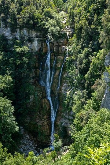 La Cascata del Rio Verde nasce nel cuore della montagna abruzzese, all'interno del Parco della Majella, un’area protetta che si estende tra le province di Pescara e Chieti. Il Rio Verde è un torrente che scorre attraverso il territorio di Guardiagrele, in particolare nella zona di Bocca di Valle, una località che si trova a circa 10 chilometri dal centro abitato del comune. Il paesaggio circostante è dominato da alture montuose, fitte foreste e formazioni rocciose, creando un ambiente naturale incontaminato dove la cascata si inserisce perfettamente. Il fiume, che prende vita dalle acque sorgive delle montagne circostanti, percorre un tratto tortuoso fino a compiere la sua spettacolare discesa. La cascata si sviluppa in più salti e si caratterizza per la sua bellezza selvaggia, con l’acqua che scivola impetuosa lungo le pareti rocciose, creando una nuvola di schiuma bianca che si diffonde nell'aria. Durante il periodo primaverile e autunnale, il flusso d'acqua è particolarmente intenso, rendendo il panorama ancora più suggestivo. L'accesso alla cascata avviene tramite un sentiero che si snoda tra il bosco e le pareti rocciose, offrendo ai visitatori un’esperienza immersiva nella natura. L’area è ben segnalata e facilmente raggiungibile anche da chi non ha molta esperienza in escursioni, ma comunque bisogna prestare attenzione agli aspetti tecnici del percorso. Il panorama che si apre durante il cammino è mozzafiato, con scorci sulla vallata sottostante e sulla vegetazione tipica di questa parte dell'Appennino. Le Cascate del Rio Verde sono un'attrazione turistica di grande fascino, non solo per la bellezza naturale, ma anche per la loro importanza storica e culturale. Infatti, la zona di Guardiagrele è ricca di tradizioni legate alla montagna e alla vita rurale, e visitare la cascata significa immergersi in un contesto che racconta la storia di questo angolo di Abruzzo. La presenza della cascata, con il suo potente flusso d’acqua e il paesaggio incontaminato, rappresenta uno dei luoghi più suggestivi di tutta la regione.