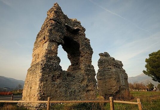 L'antica Corfinium, oggi Corfinio, si trova nella conca di Sulmona, in provincia dell'Aquila, a 345 metri di altitudine, in una posizione strategica sulla Via Valeria, che proseguiva dalla Tiburtina e collegava Roma con Ostia Aterni (l'attuale Pescara), fungendo da via di comunicazione tra il Tirreno e l'Adriatico. Il moderno paese di Corfinio ha un aspetto medievale e si erge su uno sperone roccioso, lungo la strada statale che ricalca il tracciato secolare della Via Valeria. Il centro storico di Corfinio si sviluppa intorno a Piazza Corfinio, dove le case, disposte a semicerchio, seguono la linea della cavea dell'antico teatro romano, un testimone silenzioso della grandezza del passato. Pochi chilometri prima di giungere al paese, provenendo da Roma, si può ammirare la basilica di San Pelino, sorta su un antico cimitero paleocristiano dove fu sepolto Pelino, vescovo di Brindisi e martire a Corfinium nel 350 d.C. La chiesa, riedificata nel XII secolo, conserva importanti affreschi e un ambone magnifico, commissionato dal vescovo Oderisio. Corfinium non fu solo un insediamento di grande rilevanza commerciale e militare, ma anche un importante centro politico. Durante le guerre sociali, nel 90 a.C., Corfinium divenne la capitale della Confederazione Italica, un nucleo di stato che si oppose a Roma, rappresentando il primo tentativo di unificazione politica delle popolazioni italiche. Quando Roma iniziò a espandersi, concedendo la cittadinanza latina o romana ad alcune delle popolazioni conquistate, molti popoli del centro-sud Italia si sentirono esclusi. La loro insoddisfazione culminò con la ribellione, che portò alla proclamazione di un nuovo stato, con Corfinium come capitale. Questo stato fu chiamato Italica e coniò monete proprie, cercando di organizzarsi politicamente come Roma, con consoli, un senato e altre cariche ufficiali. La guerra sociale che ne seguì fu lunga e cruenta, coinvolgendo le principali popolazioni dell’Italia centrale e meridionale, tra cui Marsi, Peligni, Sanniti e Piceni. Nonostante la forza dell'alleanza, la confederazione non riuscì a mantenere la sua autonomia a lungo. La Legge Iulia del 90 a.C., che concedeva la cittadinanza romana a gran parte dei popoli italici, segnò la fine della ribellione. Corfinium divenne un municipio romano e la Confederazione Italica fu sciolta. Tuttavia, la capitale di Corfinium, seppur breve nella sua esistenza, rimase simbolo delle aspirazioni di indipendenza e unità delle popolazioni italiche. La sconfitta della Confederazione Italica e la successiva incorporazione di Corfinium nel sistema romano non segnarono la fine del suo ruolo nella storia. Corfinium rimase un punto strategico e un’importante località durante le fasi successive della Repubblica Romana, fino a quando, nel 49 a.C., fu conquistata durante le guerre civili tra Cesare e Pompeo. Nonostante il passaggio di potere e la trasformazione della città in municipio romano, le rovine di Corfinium continuano a raccontare la storia di una delle prime grandi lotte per l'autonomia dei popoli italici, che prefigurò, seppur in modo tragico, l’unificazione dell’Italia sotto Roma. Oggi, il sito archeologico di Corfinio è testimone di quel passato ricco e complesso, offrendo una finestra sulla storia antica della regione e sulla lotta per la cittadinanza romana.