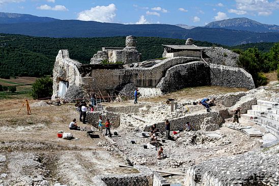 Il sito archeologico di Peltium si trova nella piana di Navelli, tra i comuni di Prata d’Ansidonia e San Pio delle Camere, e la sua fondazione risale alla metà del I secolo a.C. La città, che ebbe una notevole importanza in epoca romana, è stata oggetto di numerosi scavi a partire dagli anni '80. Le prime ricerche, condotte tra il 1983 e il 1985, hanno portato alla luce le mura di cinta nell'area meridionale del sito, gettando luce sulla struttura difensiva della città. Tra il 1986 e il 1996 sono proseguite le indagini, che hanno rivelato importanti strutture, tra cui un tratto delle mura occidentali con una porta a doppio fornice, un tempio con porticus a tre bracci e parte del teatro. Questo lavoro ha anche permesso il consolidamento delle scoperte, favorendo una maggiore comprensione del sito. Le prime indagini sono state realizzate grazie alla collaborazione tra la Soprintendenza Archeologica, l’Università degli Studi La Sapienza e altri enti locali, sotto la direzione del professor Paolo Sommella. Durante queste campagne iniziali, sono stati esplorati il tempio forense e alcune aree residenziali, ma molte strutture sono state successivamente ricoperte per preservarle, a causa delle risorse limitate destinate al restauro e alla conservazione. La ricerca ha portato alla scoperta di numerosi elementi architettonici che testimoniano la grandezza della città romana di Peltium, un'importante realtà urbanistica dell'epoca. Nel corso degli anni, altre campagne di scavo, condotte sotto la direzione di Adele Campanelli, hanno ulteriormente arricchito la comprensione del sito, rendendo visibili nuove parti delle mura e approfondendo la conoscenza del teatro. Un altro elemento di interesse è la scoperta di un apprestamento fortificato di epoca medievale, che suggerisce un'evoluzione dell'area anche dopo il declino dell'Impero Romano. Il lavoro di valorizzazione ha permesso di rendere fruibili queste strutture al pubblico, dando un'importante chiave di lettura della vita in epoca romana, così come della continuità dell'insediamento nel corso dei secoli. A partire dal 2000, le ricerche sono state riprese nell'ambito di un progetto europeo sotto la direzione di Paolo Sommella e, dal 2001, le campagne di scavo didattico sono state condotte dalla prof.ssa Luisa Migliorati. L’attenzione si è concentrata su vari aspetti della vita urbana di Peltium, inclusa la necropoli preromana situata all’esterno delle mura nord-occidentali. Le ricerche hanno permesso di ottenere nuovi dati, arricchendo il quadro storico e archeologico di questo affascinante sito. Oggi, grazie ai numerosi interventi di scavo e valorizzazione, Peltium rappresenta una delle realtà archeologiche più significative della regione, offrendo ai visitatori una visione completa della sua storia, dalla fondazione alla sua evoluzione nel corso dei secoli.