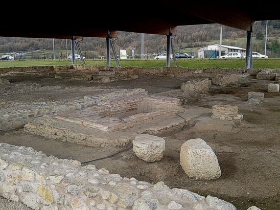 La villa romana di Avezzano è un affascinante sito archeologico situato nella periferia della moderna città di Avezzano, precisamente in località Macerine. Il sito, che si trova lungo il tracciato dell'antica via Tiburtina Valeria, è stato riportato alla luce a partire dal 2005 durante i lavori per la realizzazione di un centro commerciale. La villa, che in epoca romana faceva parte del territorio di Alba Fucens, rappresenta una testimonianza importante della vita rurale romana e delle abitazioni di campagna di quel periodo. L’area archeologica conserva i resti di un’ampia villa rustica, dove è possibile osservare vari ambienti destinati sia alla famiglia che al personale di servizio. Tra le strutture più significative c’è l’ambiente del porticato, con vasche per la spremitura e grandi buche destinate alla conservazione di olio e vino, che riflettono l'attività agricola che caratterizzava la villa. Il sito è attraversato da un ingresso e un atrio, al centro del quale si trova l'impluvium, una tipica vasca romana per la raccolta delle acque piovane, elemento fondamentale nell’architettura romana. Una delle meraviglie più celebri di questo sito è il pavimento a mosaico del triclinio, risalente al II-III secolo d.C. Il mosaico raffigura una Vittoria alata su un carro trainato da due cavalli in corsa, un simbolo di vittoria e potenza. Questo mosaico, di notevole valore artistico, testimonia l'alto livello delle decorazioni interne e l'importanza sociale ed economica della famiglia che abitava la villa. La villa fu abbandonata tra la fine del V e l'inizio del VI secolo d.C., probabilmente a causa di un forte terremoto che danneggiò la struttura. Le sepolture rinvenute lungo il perimetro della villa suggeriscono che alcuni degli ultimi abitanti siano stati sepolti nelle vicinanze, segnando la fine di un'epoca. Oggi, il sito archeologico rappresenta una risorsa fondamentale per comprendere la vita quotidiana nell'epoca romana e l'evoluzione delle strutture residenziali rurali in Abruzzo.