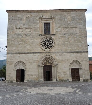 La chiesa di Santa Lucia a Magliano De’ Marsi rappresenta un importante centro di culto nella Marsica, caratterizzata da una forte connessione con il paesaggio montano che la circonda. Dedicata alla santa, la chiesa sorge in un contesto naturale di grande suggestione, con il Monte Velino che si staglia sullo sfondo, donando al luogo una carica simbolica di protezione e sacralità. La sua posizione tra le imponenti cime dell’Abruzzo contribuisce a creare un’atmosfera di quiete e devozione, ideale per la riflessione e la preghiera. Costruita nel Duecento, la chiesa ha subito nel corso dei secoli vari interventi che ne hanno arricchito l’architettura, come il rosone ogivale del Quattrocento e il finestrone tardorinascimentale aggiunto nel Seicento. Questi aggiustamenti non solo ne hanno accresciuto la bellezza, ma hanno anche testimoniato la continua crescita e il consolidamento della fede nella regione. La facciata, con i portali scolpiti da maestri francesi, evidenzia l’influenza artistica europea dell’epoca, mentre l’interno conserva intatto il suo fascino primitivo, facendo risaltare la purezza del suo spirito originario. L’interno della chiesa, con la sua divisione in tre navate, si presenta come uno spazio solenne e raccolto, dove il fedele può immergersi pienamente nell’esperienza spirituale. Le navate laterali, più basse rispetto alla centrale, sono delimitate da archi a sesto acuto, a sottolineare la verticalità e l’elevazione spirituale che caratterizzano la sacralità del luogo. I capitelli decorati delle colonne sono testimonianza della maestria dei costruttori, che hanno saputo infondere nella struttura un senso di armonia e sacralità. Nel cuore della chiesa, la vasca del fonte battesimale del Quattrocento rappresenta un ulteriore simbolo di rinnovamento spirituale. Questo elemento, legato alla tradizione cristiana, diventa il punto di passaggio verso una nuova vita nella fede, accogliendo i pellegrini e i fedeli che vi si recano in cerca di grazia e benedizione. La chiesa di Santa Lucia non è solo un luogo di culto, ma un vero e proprio simbolo di fede e resistenza, che ha attraversato i secoli mantenendo viva la sacralità del suo messaggio.