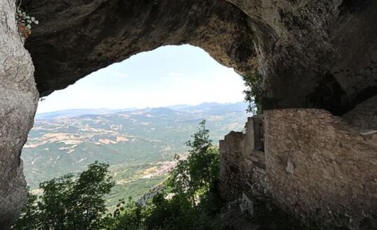 La Grotta di Sant'Angelo, situata nel comune di Lama dei Peligni in provincia di Chieti, è un affascinante sito naturale che si erge a circa 1300 metri di altitudine, oltre la località Calvario. La grotta ospita un eremo dedicato a Sant'Angelo, noto anche come San Michele, il cui interno conserva ruderi di mura e una nicchia, testimonianze della sua storica funzione religiosa. Questo luogo, immerso nella natura, ha un'atmosfera unica, grazie alla sua posizione isolata e al silenzio che lo circonda, rendendolo un punto di grande interesse sia per gli amanti della storia che per quelli della natura. L’eremo di Grotta Sant'Angelo si presenta come un grande androne di circa 20 metri di larghezza, con poche tracce di muratura che delineano la struttura originaria. L'ingresso, un tempo completamente chiuso, aveva un unico accesso centrale che conduceva all’interno, diviso in due ambienti: uno destinato alla zona presbiteriale e l'altro riservato all'abitazione dei monaci. Nonostante il passare dei secoli, l’ambiente conserva ancora l’impronta di quello che un tempo doveva essere un rifugio spirituale, immerso tra le montagne della Majella. La storia della grotta e dell’eremo risale almeno al 1447, anche se la tradizione popolare suggerisce una fondazione più antica, probabilmente risalente all'epoca altomedievale. Nel corso dei secoli, l'eremo ha avuto diverse vicissitudini, legate anche alla storia locale. Nel 1656, durante una grave epidemia di peste, il notaio De Camillis si rifugiò nel luogo per sfuggire alla malattia. Un secolo dopo, nel 1756, il ritrovamento di monete d'oro in una cavità della grotta suscitò grande curiosità, portando a un'azione di saccheggio da parte degli abitanti del luogo che distrussero parte delle mura in cerca di un tesoro nascosto. Raggiungere la Grotta di Sant'Angelo è un'avventura che richiede un po' di impegno. Partendo da Lama dei Peligni, si prosegue fino al parcheggio situato a monte del Convento di Santa Maria della Misericordia. Da lì, un sentiero ben segnato conduce attraverso i ripidi versanti della montagna, offrendo uno spettacolo suggestivo della natura circostante. Dopo circa due ore di cammino, si giunge a una cresta che immette nel vallone di Sant'Angelo. L'ultimo tratto del percorso, che passa accanto alla Fonte della Spogna, porta infine al cuore dell'eremo, immerso in un paesaggio di straordinaria bellezza.
