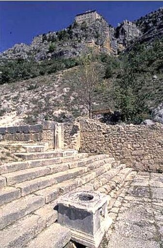 Il Santuario di Ercole Curino, situato sulla montagna Morrone, in località Badia nel comune di Sulmona, è uno dei luoghi di culto più rilevanti dell'Abruzzo. Fondato nell'età ellenistica, il sito continuò a essere utilizzato fino alla metà del II secolo d.C. e si sviluppa su terrazzamenti artificiali, che creano una successione di spazi sacri disposti lungo il pendio montano. Il santuario è un esempio notevole di architettura religiosa, caratterizzato da un grande tempio posto su un podio elevato, da un sacello monumentale con una gradinata e da un piazzale lastricato che si apre sulla panoramica conca peligna. La ristrutturazione principale del santuario avvenne all'inizio del I secolo a.C., quando venne creato un grande terrazzo inferiore sorretto da un massiccio muro in opera quasi reticolata. Su questo terrazzo furono costruiti ambienti voltati, destinati a servire la funzione sacra del luogo. Nonostante un successivo abbandono dovuto a una frana che seppellì gli edifici, il sito conservò la sua sacralità. L'arrivo del Cristianesimo non cancellò il valore spirituale dell'area, testimoniato dall'edificazione di una piccola chiesa, ampliata successivamente da Papa Celestino V nel XIII secolo. Tra i numerosi reperti emersi durante gli scavi, spicca una preziosa statuetta bronzea di Ercole, raffigurante la divinità in riposo. Questa statuetta è considerata una replica di un'opera di Lisippo, il grande scultore greco, ed è ora conservata presso il Museo Archeologico Nazionale d'Abruzzo di Chieti. Questo eccezionale reperto rappresenta non solo un'importante testimonianza della cultura materiale dell'epoca romana, ma anche un simbolo della devozione nei confronti di Ercole, divinità protettrice delle sorgenti e dei mercanti. L'accesso al sito avviene tramite un sentiero che conduce al limite settentrionale del santuario, dove si trova l'ingresso utilizzato durante la fase di ristrutturazione del I secolo a.C. Dal terrazzo mediano, i visitatori possono salire alla gradinata monumentale che porta al terrazzo superiore, dove si trovano i resti del tempio. Qui si può osservare il sacello con il pavimento musivo policromo, decorato da motivi ellenistici. Il santuario offre anche una vista spettacolare sulla conca peligna, con un paesaggio che permette di apprezzare appieno la maestosità del sito e il suo legame con il territorio circostante.