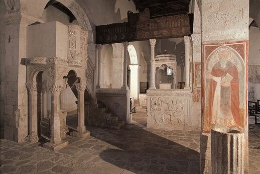I luoghi sacri in Abruzzo: La chiesa di Santa Maria in Valle Porclaneta. La chiesa di Santa Maria in Valle Porclaneta, situata nei pressi del borgo di Rosciolo, è una delle testimonianze più affascinanti del culto medievale in Abruzzo. Fondata agli inizi dell’XI secolo tra i possedimenti dell’abbazia di Montecassino, essa rappresenta un luogo di preghiera e riflessione spirituale che ha accolto fedeli per secoli. La sua posizione immersa nella quiete della valle che sfocia nella piana del Fucino conferisce al luogo un'atmosfera di tranquillità, invitando alla contemplazione e alla connessione con il divino. Il culto che si celebra in questa chiesa è profondamente legato alla tradizione benedettina, che ha avuto una grande influenza sullo sviluppo religioso della regione. Santa Maria in Valle Porclaneta non è solo un luogo di preghiera, ma anche un simbolo di continuità nella fede che si è radicata nel territorio abruzzese. Ogni angolo della chiesa testimonia l’intensità del culto che vi si è celebrato, con i suoi decorati altari e le ricche opere artistiche che ne adornano gli interni, come la transenna in pietra e l'iconostasi in legno, che separa lo spazio sacro dal mondo dei fedeli. Particolarmente rilevante è l'iconostasi, una rarità nel panorama architettonico abruzzese, che conserva ancora oggi la sua straordinaria bellezza nonostante il trascorrere dei secoli. La sua funzione, che divideva lo spazio sacro dalla parte riservata ai fedeli, ne sottolinea la sacralità e la distanza tra l’umano e il divino, un concetto fondamentale per la spiritualità benedettina. La chiesa di Santa Maria in Valle Porclaneta si presenta quindi come un luogo in cui il culto è permeato da un forte senso di separazione tra la vita terrena e quella spirituale, celebrato attraverso simboli e pratiche sacre che invitano alla riflessione. La chiesa è meta di pellegrinaggi non solo per la sua bellezza architettonica e storica, ma anche per il significato che essa riveste nel panorama religioso abruzzese. Il culto che vi si celebra rappresenta un legame profondo con la tradizione monastica e con la spiritualità che ha caratterizzato la vita religiosa in questa regione. Visitare Santa Maria in Valle Porclaneta è immergersi in un luogo che conserva un’intensa carica spirituale, dove l’arte, la storia e la fede si intrecciano in un’esperienza unica di devozione.