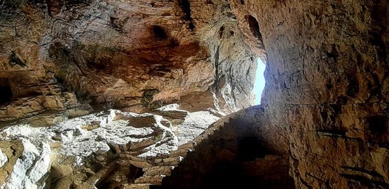 La Grotta di Sant'Angelo, situata a Civitella del Tronto, è un luogo naturale straordinario che si apre all'inizio del sentiero che conduce alle gole del Salinello. Questa grotta si distingue dalle tradizionali cavità turistiche per l'assenza di concrezionamenti come stalattiti e stalagmiti, lasciando al visitatore una visione chiara delle stratificazioni rocciose. La cavità, modellata dall'azione millenaria dell'acqua, si presenta come una naturale cattedrale gotica, illuminata da un finestrone che consente alla luce solare di entrare e creare un suggestivo gioco di luci e ombre. Questo fenomeno visivo ha affascinato l'uomo per secoli, evocando un senso di mistero e sacralità. Oltre alla sua bellezza naturale, la Grotta di Sant'Angelo ha un grande valore storico e archeologico. Un importante scavo archeologico ha rivelato un fronte stratigrafico intatto che racconta la lunga storia dell'utilizzo del sito, che risale al Neolitico e si protrae fino ai giorni nostri. Le tracce di un culto primitivo, probabilmente dedicato a Madre Terra, sono evidenti nelle strutture rinvenute all'interno della grotta, suggerendo una connessione tra il paesaggio e le pratiche spirituali delle prime popolazioni umane. Questo luogo, dunque, non è solo un rifugio naturale, ma anche un santuario della storia. Nel corso dei secoli, la grotta è stata utilizzata anche per scopi religiosi cristiani, come testimoniato dall'altare in pietra calcarea che fu posto nella grotta il 26 giugno 1236 in onore di San Michele Arcangelo. Questo altare rappresenta il punto di incontro tra il culto precristiano e quello cristiano, mostrando come la grotta abbia continuato a essere un luogo sacro, adattandosi alle diverse forme di religiosità che si sono susseguite. Il sito divenne quindi un punto di riferimento per i pellegrini e per coloro che cercavano un contatto più intimo con il divino, lontano dalle istituzioni ufficiali. Oggi, la Grotta di Sant'Angelo rappresenta un perfetto esempio di come la natura e la storia si intrecciano, offrendo uno spazio in cui l'uomo può contemplare il proprio passato e il proprio rapporto con il mondo naturale. Le tracce lasciate dagli eremiti che vi vissero per circa mille anni sono un altro elemento che rende la grotta affascinante, con le loro modeste costruzioni che si integrano perfettamente nell'ambiente circostante. Questo luogo non è solo un punto di interesse archeologico, ma anche un simbolo della spiritualità che ha attraversato i secoli, raccontando una storia di fede, natura e vita.