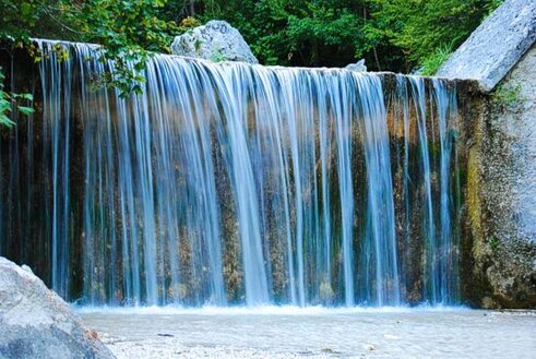 La Cascata di Vena Roscia si trova nel comune di Isola del Gran Sasso d'Italia, precisamente nella frazione di Pretara, in provincia di Teramo. Questa meravigliosa cascata nasce dal torrente Ruzzo, una delle principali sorgenti del Gran Sasso, e rappresenta una delle bellezze naturali più spettacolari del Parco Nazionale del Gran Sasso e Monti della Laga. La sua sorgente è situata a un’altitudine di 1497 metri, nella zona di Fossaceca, e crea un salto di 16 metri che si estende da una quota di 1009 metri a una di 993, formando un suggestivo paesaggio di acque che scorrono tra le pareti rocciose. Il torrente Ruzzo si snoda attraverso un’incantevole gola incisa nel massiccio calcareo del Gran Sasso, dove il suo corso crea numerosi salti e cascate. La Cascata di Vena Roscia è la più alta in quota tra quelle che si incontrano lungo il fiume, ma altre cascate lungo il suo percorso, come quelle del Mescatore e delle Coste Baroni, sono altrettanto affascinanti e contribuiscono a rendere questa zona una delle più spettacolari d’Abruzzo. Le acque del fiume scorrono tra pareti a strapiombo e creano rivoli che danno vita a scenari mozzafiato, particolarmente suggestivi per gli escursionisti. L’importanza del fiume Ruzzo non si limita alla sua bellezza naturale, ma gioca anche un ruolo fondamentale nell’approvvigionamento idrico della regione, alimentando l’acquedotto del Ruzzo, una delle opere idrauliche più rilevanti d’Abruzzo. Le sorgenti del Ruzzo sono alimentate da tre principali fonti: la Fossaceca, le Piscine e il Peschio, che forniscono acqua per l’intero sistema. Queste sorgenti si trovano in un contesto naturale di grande valore ecologico, con una vegetazione ricca e variegata, tra cui faggi, carpini e salici che crescono lungo il corso d’acqua. Per raggiungere la Cascata di Vena Roscia, si parte dalla frazione Pretara e si percorre un comodo sentiero che attraversa la zona, passando prima per il ponte sul fiume Ruzzo. Il percorso, che si snoda nel cuore del Parco Nazionale del Gran Sasso, è adatto anche a famiglie con bambini grazie alla sua facile accessibilità. Durante l’escursione, si ha la possibilità di immergersi completamente nella natura incontaminata e di ammirare la maestosità delle cascate e del paesaggio circostante, che regalano un’esperienza unica di contatto con l’ambiente montano dell’Abruzzo.