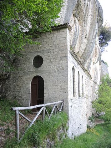 Sant’Onofrio a Serramonacesca, storia di Santi ed Eremiti nella chiesa sotto la montagna. Sant'Onofrio a Serramonacesca è un luogo di culto che affonda le radici nella tradizione eremitica e nella devozione popolare. Situato ai piedi della maestosa Majella, il santuario si erge in un'area di straordinaria bellezza naturale, immerso nel verde di un vallone che porta il suo nome. Questo eremo, che affascina per la sua posizione isolata e la semplicità della sua architettura, rappresenta un angolo di spiritualità profonda, lontano dal trambusto del mondo. La sua storia è strettamente legata alla figura di Sant'Onofrio, santo eremita noto per la sua vita ascetica, simbolo di penitenza e devozione. La chiesetta di Sant’Onofrio è un luogo che invita alla riflessione e alla preghiera, con un’atmosfera che incarna la purezza della fede. L'interno della chiesa è semplice ma suggestivo, con l’altare che si appoggia direttamente alla roccia, come se la montagna stessa fosse parte integrante del sacro. Qui, tra le pareti di pietra e il silenzio che avvolge il luogo, i pellegrini e i visitatori sono accolti da un senso di pace che sembra emanare dall'ambiente stesso. Un particolare di grande interesse è la “culla di Sant'Onofrio”, un ripiano roccioso dove la tradizione vuole che i devoti si distendano per cercare conforto nelle malattie fisiche, in un atto di fede e speranza. Il culto che si svolge a Sant'Onofrio non si limita alla preghiera, ma è anche legato a un antico rito di guarigione. La "culla" è infatti un simbolo di speranza per coloro che cercano sollievo dai propri mali, un testamento della devozione che ancora oggi anima il luogo. Questo aspetto di guarigione spirituale e fisica ha reso l'eremo una meta di pellegrinaggio, attirando coloro che, lontani dalle distrazioni della vita quotidiana, cercano un incontro profondo con il divino. La chiesetta e il paesaggio che la circonda sono diventati simboli di quella ricerca interiore che, secondo la tradizione eremitica, conduce alla purificazione dell'anima. Sant’Onofrio a Serramonacesca rappresenta, dunque, un esempio vivo di culto e spiritualità in Abruzzo, un luogo dove la storia degli eremiti e dei santi si fonde con la sacralità della natura circostante. Sebbene poco conosciuto al grande pubblico, l’eremo è un punto di riferimento importante per chi desidera entrare in contatto con la tradizione religiosa più autentica e profonda. La sua solitudine e la sua bellezza selvaggia offrono un'opportunità unica di riflessione e di preghiera, un invito a riscoprire il legame indissolubile tra la fede e la natura.