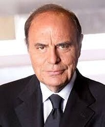 Bruno Paolo Vespa (L'Aquila, 27 maggio 1944) è un giornalista, conduttore televisivo, autore televisivo e scrittore italiano. Bruno Paolo Vespa, nato a L’Aquila il 27 maggio 1944, è una figura di spicco nel panorama del giornalismo italiano, che ha saputo costruire una carriera ricca di successi e di riconoscimenti. La sua attività si è sviluppata attraverso una pluralità di ruoli, tra cui giornalista, conduttore televisivo, saggista e autore, portando il suo nome e il prestigio della sua terra d’origine, l’Abruzzo, a livello nazionale e internazionale. Sin dai suoi esordi, Vespa ha mostrato una passione per l’informazione che lo ha portato a esplorare e innovare diversi ambiti della comunicazione, lasciando un’impronta indelebile nella storia del giornalismo italiano. L’attività di Bruno Vespa è iniziata a soli sedici anni, quando collaborava con la stampa locale abruzzese. Poco dopo, entrò in Rai come cronista radiofonico e, a partire dal 1968, iniziò a lavorare nel mondo della televisione dopo aver conseguito la laurea in Giurisprudenza alla Sapienza di Roma. Vespa si distinse subito per il suo approccio rigoroso e la capacità di affrontare temi complessi con chiarezza e precisione. Nel corso della sua carriera come inviato speciale del TG1, ha coperto eventi di rilevanza storica, come la strage di Piazza Fontana nel 1969, dimostrando un talento straordinario nella narrazione degli avvenimenti di cronaca e politica. L’attività televisiva di Vespa raggiunse il suo massimo splendore con la creazione di Porta a Porta, il programma di approfondimento politico e culturale che conduce su Rai 1 dal 1996. Questa trasmissione, definita ironicamente “la terza camera del Parlamento” da Giulio Andreotti, ha rappresentato un luogo di confronto e dibattito sui principali temi dell’attualità italiana. Vespa si è distinto come moderatore in momenti cruciali della storia politica del Paese, come i confronti elettorali tra leader politici e l’ormai celebre puntata in cui Silvio Berlusconi firmò il “Contratto con gli italiani” nel 2001. Oltre alla televisione, Vespa ha sviluppato un’intensa attività editoriale. È autore di numerosi saggi e libri di analisi politica e storica, che lo hanno reso uno degli intellettuali più influenti del panorama italiano. Ha collaborato con importanti testate giornalistiche, tra cui Il Mattino e Il Gazzettino, oltre a dirigere, dal 2014 al 2019, il consorzio QN-Quotidiano Nazionale. La sua voce autorevole ha contribuito a plasmare l’opinione pubblica, offrendo spunti di riflessione su temi di grande rilevanza sociale e politica. L’attività di Vespa è sempre stata legata al suo amore per l’Abruzzo. La sua terra d’origine è stata protagonista di molte sue narrazioni, in particolare in occasione del terremoto del 2009 che colpì L’Aquila. Attraverso il suo programma Porta a Porta e altre iniziative mediatiche, Vespa ha dato voce alle difficoltà e alle speranze della sua comunità, rafforzando il legame con le sue radici. Con il suo lavoro, Bruno Vespa ha portato lustro all’Abruzzo, rendendolo parte integrante della sua identità e della sua carriera di successo.