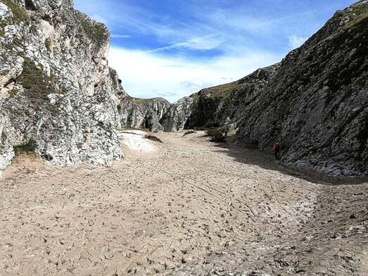 Trekking nelle Gole naturali in Abruzzo: Gole dello Scoppaturo. Le Gole dello Scoppaturo si trovano nel cuore dell’Abruzzo, nella piana di Campo Imperatore, un altopiano che offre paesaggi unici e scenari naturali straordinari. Questo canyon, noto anche come Canyon della Valianera, si sviluppa lungo il letto di un antico fiume che scorreva un tempo nell'area. L'accesso al canyon è facilmente individuabile lungo la SS 17bis, che attraversa la piana e prosegue verso Fonte Vetica. L’escursione, che dura circa un'ora e mezza per una distanza di circa 4 km, consente di immergersi in un mondo a parte, lontano dalle caratteristiche dell’altipiano circostante. Camminando tra le pareti rocciose, il paesaggio appare come un'opera scolpita dalla natura, tra rocce che si avvicinano e si allontanano creando un percorso che si restringe e si espande, dando l’impressione di essere in un altro mondo. Il fascino delle Gole dello Scoppaturo è proprio nel suo paesaggio drammatico e quasi lunare, dove le forze naturali hanno scolpito le rocce nel corso dei secoli. Un tempo, l’altopiano di Campo Imperatore era ricoperto dai ghiacciai, che hanno modellato la terra, lasciando dietro di sé una serie di massi e formazioni rocciose che dominano l’ambiente circostante. L’escursione offre panorami mozzafiato a 360 gradi, dove ogni angolo del canyon racconta una storia di geologia, evoluzione e bellezza. Ogni passo lungo il sentiero consente di ammirare la grandezza e la potenza della natura, in un paesaggio che sembra essersi fermato nel tempo. La flora e la fauna che abitano le gole sono un altro degli aspetti che rendono questa escursione unica. Lungo il sentiero, si possono osservare piante che resistono alle difficili condizioni ambientali, come le piante grasse, che crescono tra le rocce. Alcune di esse sembrano quasi danzare al vento, aggiungendo colore e vita a un ambiente che, altrimenti, apparirebbe arido e inospitale. Durante la stagione primaverile, la vegetazione spontanea colora il paesaggio, con fioriture che contrastano con la durezza della pietra. Inoltre, non è raro avvistare alcune specie di animali, come il camoscio appenninico, che abita questi luoghi impervi. Il camminatore più attento potrà anche ascoltare i suoni che caratterizzano l'ambiente naturale delle gole: il vento che soffia tra le alte pareti rocciose, il canto degli uccelli come le cornacchie e i gracchi, e il suono sordo dei passi sulla pietra. Questi suoni, uniti alla bellezza selvaggia del paesaggio, creano un’atmosfera magica, in cui il silenzio e la pace regnano sovrani. La sensazione di solitudine e tranquillità, lontano dalla frenesia della vita quotidiana, rende questa escursione un’esperienza immersiva che nutre l’anima e offre un’opportunità di connessione profonda con la natura. Proseguendo nel percorso, il paesaggio cambia, evolvendosi in modo sorprendente. All’inizio, le gole sono strette e incassate, con le pareti rocciose che si sfiorano quasi a formare un passaggio angusto. Ma man mano che si prosegue, il canyon si apre, dando spazio a valloni più ampi e panoramici. In questo tratto, i ghiaioni residui dell'era glaciale cedono il posto a ampi prati ricchi di piante e fiori, tra cui la genziana, simbolo di Campo Imperatore. Questo contrasto tra l’aridità iniziale e la vegetazione che lentamente prende piede nel canyon rende l’escursione ancora più affascinante, come se si stesse vivendo un viaggio attraverso diverse dimensioni naturali.