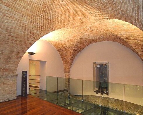 La Casa dei Melatino di Teramo è un affascinante esempio di architettura storica che ha radici nel XIII secolo, con la sua costruzione risalente al 1232. L’edificio ha subito diverse modifiche nel corso dei secoli, come si evince dalla stratigrafia muraria, che documenta le varie fasi di evoluzione. La struttura, che si sviluppa su tre piani, è caratterizzata da una pianta quadrata e irregolare, con una facciata principale che si affaccia sulla strada e una seconda facciata che si apre su un giardino interno. Sebbene i lati corti dell’edificio siano stati successivamente occupati da edifici più recenti, l’edificio originariamente era isolato, come testimoniano le cronache locali. La facciata della Casa dei Melatino rivela alcuni dettagli architettonici interessanti, che suggeriscono un rifacimento o ristrutturazione dell’edificio in un periodo di grande prosperità per la città. Le finestre disposte in serie sono una delle caratteristiche principali della facciata, con alcune che presentano una colonnina divisoria centrale. Un esempio particolarmente singolare è una finestra con una colonnina ottagonale, che poggia su una base da cui emerge un volto umano ormai deteriorato, e un capitello decorato con motivi floreali. Altre finestre sono adornate con colonnine che recano scolpiti volti maschili e femminili, e in una di esse un corpo serpentino che si avvolge lungo il fusto della colonna, con capitelli arricchiti da foglie e fiori. Al piano terra, l’edificio ospita tracce di diverse epoche, che spaziano dal periodo medievale a quello rinascimentale, ma anche resti di strutture romane. Un elemento di particolare interesse sono i pavimenti in mosaico, in marmo bianco e policromo con inserti di pietra lavica, che testimoniano l’uso raffinato di materiali pregiati nell’antica domus romana che occupava questa zona. Inoltre, alcuni tratti di intonaci dipinti ci permettono di immaginare l’aspetto originario dell’edificio, arricchito da decorazioni che parlano di un passato ricco di arte e cultura. Oggi, la Casa dei Melatino ospita una collezione di maioliche antiche abruzzesi di grande valore, insieme a porcellane europee di pregio. Le maioliche, in particolare, rappresentano un’importante tradizione artigianale della regione, che si è sviluppata nel corso dei secoli e che costituisce uno dei tratti distintivi del patrimonio artistico abruzzese. La casa, quindi, non è solo un luogo di interesse storico e architettonico, ma anche un punto di riferimento per la conservazione e la valorizzazione delle tradizioni artistiche e culturali dell’Abruzzo.