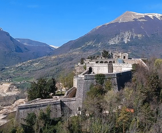 Civitella del Tronto e la sua Fortezza. Civitella del Tronto sorge su un’imponente altura che domina il fiume Tronto, antico confine tra il Regno di Napoli e lo Stato Pontificio, oggi spartiacque tra Abruzzo e Marche. La sua fortezza, tra le più grandi d’Europa, ha origini medievali ma assume la sua forma attuale tra il XVI e il XVII secolo, quando diventa un baluardo strategico del Regno di Napoli. La sua storia è segnata da assedi e battaglie, culminando nell’episodio drammatico del 1860-61, quando l’ultima guarnigione borbonica si arrese all’esercito sabaudo, sancendo la definitiva unificazione dell’Italia. L’ingresso al borgo avviene attraverso una porta duecentesca che introduce nel cuore del centro storico, caratterizzato da vicoli stretti e suggestivi, su cui si affacciano antichi edifici e chiese di grande valore artistico. Salendo verso la fortezza, il panorama si apre sulle colline circostanti, offrendo scorci spettacolari che accompagnano il visitatore fino alle poderose mura difensive. Ogni passo racconta storie di soldati e comandanti, di strategie e sacrifici, in un luogo che per secoli ha rappresentato il confine tra due mondi. All’interno della fortezza si respira l’atmosfera del passato, tra gli ampi spazi della Piazza d’Armi, un tempo centro nevralgico della vita militare, e le postazioni di difesa, tra cui il Bastione di San Giacomo, da cui si gode una vista mozzafiato. Il Palazzo del Governatore, che un tempo ospitava il comando della guarnigione, conserva ancora il fascino austero di un’epoca in cui ogni dettaglio architettonico rispondeva a precise esigenze difensive. Oggi, la fortezza è un luogo di memoria e cultura, con le sue antiche caserme che ospitano un museo dedicato alla sua storia e all’assedio del 1860-61. Attraverso reperti, mappe e ricostruzioni, il visitatore può ripercorrere le vicende che hanno segnato la fine del dominio borbonico. Immersa in un paesaggio di straordinaria bellezza, Civitella del Tronto resta una delle più affascinanti testimonianze storiche dell’Abruzzo, un luogo dove la storia si fonde con la suggestione del territorio.