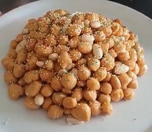 La preparazione della Cicerchiata, dolce tipico della provincia di Pescara, inizia con la creazione dell’impasto, che rappresenta il cuore della ricetta. Si mescolano farina e uova fresche, ingredienti semplici ma fondamentali della cucina abruzzese, con un po’ di zucchero e burro, entrambi provenienti da prodotti locali. L'impasto ottenuto deve essere lavorato fino a raggiungere una consistenza morbida ma compatta, pronta per essere modellata. Il burro, spesso di produzione artigianale, conferisce una ricchezza e una morbidezza che, una volta fritte, si trasformano in una croccantezza irresistibile. Una volta pronto l'impasto, si procede a formare piccole palline, che vengono poi fritte in abbondante olio caldo. L'olio utilizzato, preferibilmente d'oliva, è un altro ingrediente tipico della cucina abruzzese, che dona un sapore delicato e genuino al dolce, senza coprire gli altri aromi. La frittura deve essere lenta e costante, in modo che ogni pallina diventi dorata e croccante all'esterno, mentre all'interno rimane morbida. Il contrasto tra l’interno morbido e la croccantezza esterna è uno degli aspetti che rende la Cicerchiata tanto amata. Una volta fritte, le palline di pasta vengono immerse in miele caldo, che lega il tutto con il suo dolce e aromatico sapore. Il miele, proveniente dalle colline abruzzesi, spesso di acacia o millefiori, dona una nota avvolgente e profumata, che si sposa perfettamente con la croccantezza delle palline. L’uso di miele locale è essenziale per ottenere quel sapore autentico che rende la Cicerchiata un dolce inconfondibile. Il miele si fonde con le palline, creando una copertura dolce e lucente che avvolge ogni morso in un caldo abbraccio. Infine, la Cicerchiata viene decorata con zuccherini colorati o mandorle tritate, aggiungendo un tocco di colore e croccantezza. La mandorla, un altro ingrediente tipico dell'Abruzzo, arricchisce il dolce con una nota leggermente amara che bilancia la dolcezza del miele. Il risultato finale è un dolce che rappresenta perfettamente la tradizione abruzzese, unendo ingredienti semplici ma ricchi di sapore che raccontano la storia e la cultura di questa terra. La Cicerchiata è così pronta per essere gustata, portando con sé tutta l’autenticità della cucina abruzzese.
