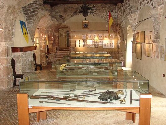 La Fortezza Museo delle Armi di Civitella del Tronto, situato all’interno dell’imponente fortezza che domina il borgo, è un luogo che racconta la storia militare e difensiva del territorio attraverso una vasta collezione di armi storiche. Fondato nel 1988, il museo si sviluppa su due piani ed è stato allestito in quello che un tempo era un magazzino dell’artiglieria. Qui i visitatori possono ammirare una serie di pezzi significativi, tra cui due falconetti da marina del Seicento, un obice del Settecento e vari cannoni da campagna, insieme a palle di cannone originali ritrovate durante i lavori di restauro, offrendo uno spunto affascinante sul passato bellico della zona. Al primo piano, il museo è organizzato in quattro sale tematiche, ognuna delle quali racconta un capitolo specifico della storia. La prima sala, dedicata al benefattore Giorgio Cucentrentoli di Monteloro, ospita una serie di oggetti legati alla storia risorgimentale, come ritratti di Savoia, Cavour e Garibaldi, oltre a documenti storici e uniformi, tra cui un elmo e una divisa dello Stato Pontificio. La sala successiva è interamente riservata alla memoria del Risorgimento e raccoglie armi appartenenti sia all’esercito sardo-piemontese che a quello borbonico, come baionette, fucili, sciabole e pistole, testimonianze di uno dei periodi più cruciali della storia italiana. Nel percorso espositivo, la terza sala ospita un interessante cippo confinario, una colonna di pietra che segnava il confine tra il Regno delle Due Sicilie e lo Stato Pontificio nel 1846-47. Il cippo, decorato con il giglio dei Borbone e le chiavi incrociate del Papato, rappresenta un’importante testimonianza delle divisioni territoriali dell’epoca. La quarta sala è invece dedicata alle armi più antiche, con esemplari risalenti al Rinascimento, tra cui schioppi a miccia del Quattrocento e pistole a pietra focaia del Settecento. Le pareti sono adornate con riproduzioni di mappe storiche, che offrono un’affascinante visione della fortezza e del borgo nei secoli passati. La visita al Fortezza Museo delle Armi è un’esperienza che permette di immergersi nella storia di Civitella del Tronto e del suo ruolo strategico. Non solo gli oggetti esposti raccontano storie di battaglie e di guerre, ma anche la posizione della fortezza, che ha resistito a numerosi assedi, diventa un importante elemento di riflessione sulla difesa del territorio. Il museo rappresenta una meta imperdibile per chi desidera esplorare la storia militare del luogo e scoprire l’evoluzione delle tecniche di difesa e delle armi nel corso dei secoli.