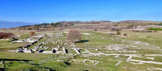 Trekking nelle valli dell’Abruzzo: Sui colli di Juvanum. L'area archeologica di Juvanum, situata nei pressi del borgo di Montenerodomo, si affaccia su un panorama straordinario che spazia sul versante orientale della Majella. Questo antico sito, che fu un'importante città italico-romana, è un luogo dove storia, natura e paesaggio si fondono in modo affascinante. Gli scavi archeologici, che si estendono su ampi pendii erbosi che circondano l'acropoli, rivelano una città che, seppur immersa nella quiete contemporanea, testimonia la vivacità e la grandezza di un passato lontano. Il cuore dell'area archeologica è rappresentato dai due tempietti gemelli, unici nel loro genere, che probabilmente erano dedicati a Ercole e ad altre divinità. Questi edifici sacri sono collegati da una strada lastricata che conduce al foro, il centro vitale della città. Al centro del foro, si ergeva una basilica dedicata al culto dell'imperatore, simbolo della devozione imperiale. Le rovine delle possenti mura che circondano l’acropoli ci raccontano dell'importanza strategica e religiosa di Juvanum, un insediamento che giocava un ruolo fondamentale nella regione. Poco lontano dall'area sacra, si trova la cavea del teatro, una struttura che offre una vista panoramica mozzafiato. Il teatro, perfettamente integrato nel paesaggio, era il luogo per eccellenza di spettacoli e rappresentazioni pubbliche, testimoniando il fervore culturale e sociale della città. La sua posizione privilegiata, che domina la vallata sottostante, rendeva l'esperienza teatrale ancora più suggestiva per gli spettatori dell'epoca, che potevano godere di un'atmosfera unica, immersi nella bellezza naturale del luogo. Oggi, la valle di Juvanum è una meta ideale per escursioni in bicicletta, a piedi o a cavallo, unendo l'emozione di un viaggio nel passato alla scoperta di panorami mozzafiato. I sentieri che si snodano tra le rovine archeologiche e il paesaggio circostante offrono l'opportunità di vivere un'esperienza che fonde storia, natura e cultura, permettendo di esplorare un luogo che è testimone di un'antica civiltà e di una bellezza paesaggistica senza pari.