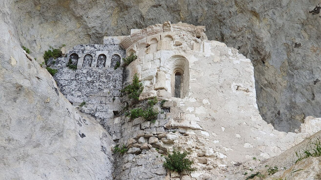 Le Grotte naturali in Abruzzo: Grotta Sant’Angelo di Palombaro. La Grotta di Sant'Angelo si trova in un suggestivo angolo della valle di Sant'Agata d'Ugno, nel comune di Palombaro, in provincia di Chieti. L'area è nota per la presenza di numerose grotte naturali, ma quella di Sant'Angelo è particolarmente significativa sia dal punto di vista storico che religioso. Sebbene la sua data di costruzione non sia certissima, si ritiene che l'eremo sia stato edificato nell'XI secolo sui resti di un antico santuario dedicato a Bona, la dea della fertilità. La prima testimonianza documentata dell'eremo risale al 1221, quando Papa Onorio III lo confermò come parte delle proprietà dell'abbazia di San Martino in Valle. La grotta che ospita l'eremo ha una forma rettangolare e si estende per circa 35 metri. Al suo interno, si può ammirare un ambiente naturale che ospita i resti di una chiesa medievale, costituita da due muri che si raccordano con un’abside semicircolare. La parte interna della grotta presenta gradini irregolari e diversi resti di cisterne, che servivano per la raccolta dell'acqua piovana. Questi elementi evidenziano come la grotta fosse un luogo autosufficiente, capace di supportare la vita monastica in passato. Le mura della grotta, insieme all'abside, sono decorati da una serie di archetti pensili, con una cornice a tortiglioni che decora anche la finestra a strombo dell'abside stesso. Questi ornamenti sono simili a quelli che si trovano nell'abbazia di San Liberatore a Majella, il che suggerisce che siano stati realizzati dalle stesse maestranze. Queste decorazioni aggiungono un ulteriore fascino alla grotta, facendo di Sant'Angelo un luogo di grande valore storico e artistico. Per raggiungere la Grotta di Sant'Angelo, è necessario percorrere un sentiero che parte dall'area attrezzata di Sant'Agata d'Ugno, un cammino di circa 15 minuti che si snoda tra la vegetazione. Il sentiero è ben protetto da una staccionata e attrezzato con scalini nei tratti più scoscesi, rendendo l'accesso sicuro anche per i visitatori. Una volta giunti alla grotta, è possibile godere di una vista spettacolare e di un'atmosfera unica, che mescola natura, spiritualità e storia.