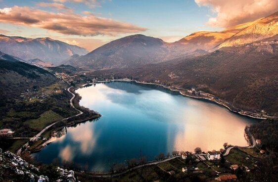 Parchi Naturali, boschi e Trekking: Scanno e il suo Lago. Scanno e il suo Lago. Scanno, con il suo affascinante borgo medievale, è una delle perle più suggestive dell'Abruzzo. Il paese, che si sviluppa tra vicoli stretti e piazze pittoresche, è un intricato mosaico di stili architettonici che spaziano dal medievale al rinascimentale e al barocco. Passeggiando per il centro storico, si può ammirare l’armonia delle case addossate le une alle altre e le magnifiche chiese che testimoniano la ricca storia di questa località. Le tradizioni locali sono ancora vive, e spesso ci si imbatte nelle anziane del paese, vestite con i caratteristici costumi tradizionali di probabile origine montenegrina, che contribuiscono al fascino immutato del borgo. L'artigianato di Scanno rappresenta un altro importante richiamo per i visitatori. Le mani esperte degli artigiani locali creano lavori unici, come pizzi fatti al tombolo e gioielli in filigrana, che raccontano la storia e le tradizioni del luogo. Oggetti come centrini, tovaglie, ciondoli e anelli sono realizzati con grande maestria e sono la testimonianza di una cultura che ha saputo preservare le sue radici nel tempo. Chi visita Scanno può portare a casa un pezzo di questa tradizione, acquistando autentici souvenir da portare con sé. Ai piedi del borgo, incorniciato dalle montagne, si trova il lago di Scanno, un autentico gioiello naturale. Il lago, che si estende a 922 metri di altitudine, è il risultato di una frana proveniente dal Monte Genzana che ha ostruito la valle del Sagittario, creando un bacino dalle acque cristalline. La bellezza paesaggistica del lago, con le sue acque tranquille e il panorama mozzafiato, attira ogni anno numerosi visitatori in cerca di pace e di un contatto diretto con la natura. È un luogo ideale per trascorrere momenti di relax, praticare il birdwatching o semplicemente godersi la tranquillità del paesaggio circostante. Negli ultimi anni, il lago di Scanno ha visto crescere la propria popolarità come meta turistica. Accanto alla tradizionale presenza di pescatori, che si dedicano alla pesca sportiva sulle sue rive o in barca, il lago è diventato un punto di ritrovo per gli amanti degli sport acquatici, come il canottaggio e il kayak. La sua natura incontaminata lo rende un luogo perfetto anche per chi cerca frescura durante le calde estati abruzzesi, e la varietà di attività che offre lo rende una destinazione ideale per tutti, dai turisti più tranquilli a quelli più dinamici in cerca di avventura.