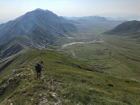 Trekking in Abruzzo: La Piana di Campo Imperatore. Nel cuore dell’Abruzzo, immersa nel maestoso Parco Nazionale del Gran Sasso e Monti della Laga, si estende la magnifica Piana di Campo Imperatore, un altopiano spettacolare che regala scenari di straordinaria bellezza. Conosciuto come il "Piccolo Tibet" per la sua vastità e l’atmosfera selvaggia, questo luogo offre percorsi di trekking adatti a tutti, permettendo di esplorare praterie sconfinate incorniciate da imponenti vette rocciose. Il silenzio avvolgente e la sensazione di trovarsi in uno spazio infinito rendono ogni passo un’esperienza immersiva e rigenerante. Il trekking a Campo Imperatore è un'ottima scelta per chi desidera scoprire la montagna senza affrontare difficoltà estreme. I sentieri attraversano morbidi pendii erbosi e si inoltrano tra distese punteggiate di fiori selvatici, offrendo un percorso che varia a seconda della stagione. In primavera, il verde brillante della vegetazione si accende di colori vivaci, mentre in autunno le tonalità dorate dipingono il paesaggio di un fascino malinconico e suggestivo. La facilità del tracciato lo rende ideale anche per famiglie e camminatori meno esperti, senza rinunciare a panorami straordinari. Salendo lungo il sentiero, si raggiunge uno dei punti più iconici del percorso: il Rifugio Duca degli Abruzzi. Situato a oltre duemila metri di altitudine, questo storico rifugio rappresenta un luogo di sosta perfetto per ammirare la vista sul Corno Grande, la vetta più alta degli Appennini. Da qui, lo sguardo può spaziare fino alla valle sottostante, regalando un colpo d’occhio che lascia senza fiato. L'aria pura e il silenzio interrotto solo dal soffio del vento creano un’atmosfera magica, difficile da dimenticare. Il percorso offre anche l’opportunità di avvistare la ricca fauna locale, che popola questa terra ancora incontaminata. Camosci appenninici, aquile reali e falchi pellegrini si muovono con eleganza tra le rocce e i cieli tersi, mentre la flora varia con l’altitudine, regalando incontri con specie rare e affascinanti. L’escursionista più attento potrà scorgere anche tracce del lupo appenninico, abitante silenzioso e simbolo della natura selvaggia di queste montagne. Al termine dell’escursione, la luce dorata del tramonto avvolge la Piana di Campo Imperatore in un’atmosfera irreale, trasformando il paesaggio in un quadro vivente. Che sia un’escursione breve o un’avventura più lunga, il trekking in questo angolo di Abruzzo offre un’esperienza che va oltre la semplice camminata: è un viaggio attraverso spazi sconfinati, storia e natura, un incontro profondo con l’anima più autentica della montagna.