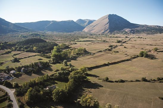 Trekking negli Altopiani e Pianori in Abruzzo: Fare trekking a Piano delle Rocche. L'Altopiano delle Rocche, situato tra le imponenti catene montuose del Sirente e del Velino, rappresenta una delle aree più suggestive dell'Appennino centrale. Con un'altitudine compresa tra i 1.200 e i 1.400 metri, questo vasto pianoro offre un ambiente incontaminato, caratterizzato da dolci rilievi, boschi di faggi secolari e ampie distese erbose che si estendono fino alle vette che lo circondano, come il Monte Rotondo, il Monte Cagno, il Monte Ocre e il Cefalone, tutte oltre i 2.000 metri. La natura qui si esprime con una forza straordinaria, regalando panorami sempre diversi a seconda della stagione e rendendo il trekking un’esperienza unica per chi desidera esplorare paesaggi di rara bellezza. Durante l’inverno, l'altopiano si trasforma in un autentico paradiso per gli appassionati degli sport sulla neve, con itinerari ideali per lo sci di fondo, lo sci escursionistico e le ciaspolate tra scenari fiabeschi. Quando la neve si scioglie e lascia spazio ai colori della primavera e dell’estate, il territorio si anima di una straordinaria biodiversità, offrendo percorsi che attraversano praterie in fiore, boschi rigogliosi e alture panoramiche. Trekking, escursioni a cavallo e tour in mountain bike diventano le attività perfette per chi vuole immergersi nella natura e scoprire il fascino di questi luoghi, camminando lungo sentieri che rivelano scorci mozzafiato su vallate incontaminate e piccoli borghi che raccontano secoli di storia e tradizioni. Uno degli spettacoli più affascinanti dell'Altopiano delle Rocche è la fioritura spontanea del narciso, che tra maggio e giugno trasforma il paesaggio in un mare bianco profumato. Questo fenomeno naturale è celebrato con la tradizionale Festa del Narciso a Rocca di Mezzo, dove carri allegorici decorati con migliaia di fiori sfilano per le strade in un tripudio di colori e creatività. Questo evento, oltre a rappresentare un momento di festa per la comunità locale, attira visitatori e appassionati di botanica da ogni parte d’Italia, offrendo un’occasione unica per ammirare la bellezza spontanea e selvaggia di questo altopiano. L'altopiano non è solo un luogo di grande interesse naturalistico, ma anche un territorio carico di storia e cultura. Le sue valli e i suoi borghi hanno ospitato celebri produzioni cinematografiche, tra cui La Strada di Federico Fellini, girato tra Ovindoli e Rocca di Mezzo, e Il ritorno di Don Camillo, ambientato a Rocca di Cambio. Questi luoghi, scelti per il loro fascino autentico e senza tempo, custodiscono memorie di epoche passate e tradizioni ancora vive, che si possono riscoprire passeggiando tra le antiche strade di pietra o visitando i piccoli santuari nascosti tra le montagne. Fare trekking a Piano delle Rocche significa immergersi in un ambiente straordinario, dove ogni sentiero racconta una storia e ogni panorama regala emozioni uniche. È un’esperienza che permette di riscoprire il contatto autentico con la natura, di lasciarsi sorprendere dalla varietà di paesaggi e di vivere un’avventura tra le meraviglie dell’Appennino abruzzese. Chiunque percorra questi luoghi, tra il silenzio delle vette e il profumo della terra, porta con sé il ricordo di un viaggio indimenticabile, fatto di passi lenti, orizzonti infiniti e una bellezza che si imprime nell’anima.