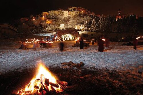 Il Presepe Vivente di Rivisondoli, il più noto d’Abruzzo, ebbe origine nell’immediato dopoguerra, nello scenario delle rovine ancora fumanti e della volontà di rinascita della fine degli anni ’40. Fu in questo quadro che le autorità cittadine dell’epoca, riunitesi per elaborare qualche progetto che desse impulso alla ripresa economica del paese, aderirono con entusiasmo ad un’idea del giornalista Renato Caniglia, di origine rivisondolese. La posizione di Rivisondoli, alle pendici di Monte Calvario, è da “presepe”. Perché non animare allora questo scenario con una rappresentazione “vivente” della Natività? La realizzazione dell’idea presentava però molte difficoltà ed impegno finanziario gravoso, soprattutto in considerazione del momento storico. Ma il progetto riuscì infine a superare gli ostacoli, cosicché nel giorno dell’Epifania del 1951 fu possibile realizzare la prima edizione del Presepe Vivente di Rivisondoli. La prima sacra rappresentazione ebbe luogo sul sagrato della chiesa parrocchiale, in uno spazio limitato che poteva accogliere pochi spettatori. Ma l’atmosfera raccolta e la rievocazione della Natività attraverso i suoi episodi salienti suscitarono nell’animo dei presenti un’emozione profonda. Un’emozione che da allora, trascorso ben oltre mezzo secolo, ogni anno si rinnova. Negli anni successivi la rappresentazione s’ampliò, si arricchì di personaggi, figuranti, scenografie, spostandosi alla base del paese in modo che l’intero abitato facesse da quinta scenografica alla rappresentazione. Ogni anno, alla vigilia dell’evento, il fervore dei preparativi prendeva tutti. Le donne confezionavano gli abiti adatti all’occasione, i bambini si vestivano da pastorelli, i vecchi pastori recuperavano i tradizionali addobbi, i giovani che dovevano impersonare soldati romani, Magi o angeli si preparavano con lo scrupolo e la serietà imposta dal ruolo. Tutto il paese aveva l’aria di un palcoscenico sul quale attori provavano le parti loro assegnate, con una gioia disinteressata e solidale quale può dare solo un evento che coinvolge l’anima e i sentimenti più genuini. Molto tempo è passato dal lontano 1951; ad opera di vari registi si è migliorata la scenografia, si sono impiegate più moderne tecniche per gli effetti delle luci e dei suoni, si sono arricchiti i costumi e gli abbigliamenti, i partecipanti (anche non rivisondolesi) sono cresciuti di numero, la scelta della ragazza per il ruolo di Madonna viene effettuata, il giorno 8 Dicembre, con il concorso “Selezione della Madonnina” , mentre il ruolo di Bambinello sarà sempre “riservato” all’ultimo nato del paese, quasi per non recidere quel cordone ombelicale che lega indissolubilmente Rivisondoli al suo Presepe Vivente.