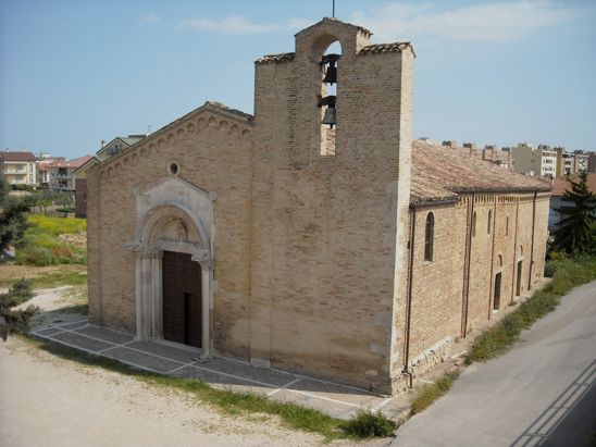 La Chiesa di Santa Maria a Mare a Giulianova. La chiesa medievale di Santa Maria a Mare è il vero gioiello artistico di Giulianova e si trova nei pressi del cavalcavia che costituisce l’accesso alla città da sud, o da Teramo. Tutta in mattoni, con un bel campanile a vela, venne costruita prima dell’anno Mille in una posizione insolita, sulla piana tra la costa e la collina lontano dal centro abitato dell’antica Castel San Flaviano, la Giulianova dell’epoca. Si pensa fosse collegata ad un punto di sosta per i viandanti che dall’interno si recavano sul mare per cercare imbarchi. Fu modificata più volte, di sicuro attorno al XII secolo, e alla fine del 1200 il vescovo affidò la realizzazione di un nuovo portale a una bottega di scalpellini, forte evidentemente di qualche bravo maestro a giudicare dal risultato. Alcuni hanno immaginato che qui avesse lavorato Raimondo del Podio, mastro scalpellino ed architetto divenuto famoso perché autore dei portali della cattedrale di Atri, ma è una ipotesi tanto suggestiva quanto poco fondata sui fatti. Al contrario, probabilmente la bottega scalpellina di Giulianova costruì poi il portale della chiesa di Colle Romano a Penne, e qui le somiglianze stilistiche sono evidenti. Santa Maria a Mare colpisce il visitatore per il suo portale, nella cui pietra sono cesellati una bellissima Madonna con Bambino contornata da animali, figure e oggetti dal significato simbolico: si distinguono infatti un’aquila ed un falco, una salamandra, una colomba, un essere mostruoso. Due leoni guardano maestosi il visitatore dai due lati del portale, uno con un libro, l’altro in lotta con un serpente. Osservando il sottoarco giunge la sorpresa: si scoprono infatti le 18 formelle di pietra che recano scolpite figure enigmatiche, volti e simboli. Difficile dire cosa narrino; di certo una storia scritta per segni, un percorso che si snoda attraverso simboli antichi, forse una rappresentazione delle fasi dello zodiaco, delle stagioni e dell’alternarsi tra la notte e il giorno con il percorso del sole tra aurora, alba, luce, tramonto, crepuscolo e buio. Tra esse alcune colpiscono la fantasia più di altre. Un uomo mostra le parti intime: una decorazione simile si segnala sul portale del duomo di Parma, opera del maestro Benedetto Antelami. Potrebbe simboleggiare l’inizio di un nuovo ciclo. Chiesa Santa Maria a Mare. Un guerriero a cavallo calpesta il drago: raffigurazione classica di San Giorgio o dell’arcangelo Michele. Il cavaliere è spesso usato come simbolo dell’uomo teso verso grandi sfide e grandi ideali, qui forse a identificare la forza della primavera. Un re che nutre delle colombe: collocata dopo alcune teste umane e una doppia stella a 12 punte, potrebbe rappresentare il possessore di conoscenza che dona il proprio sapere e quindi la vita stessa; forse uní allegoria dell’estate. Un uomo cavalca un drago: pur se mancante di una sezione inferiore che poteva contenere una raffigurazione del mare, la formella dovrebbe rappresentare il passaggio metaforico dal buio alla luce. Un giovane che ride su una maschera: segue la figura del giovane, forse un eroe. Da alcuni ritenuto una raffigurazione oscena: potrebbe trattarsi di un giovane i cui attributi maschili siano stati cancellati dagli agenti atmosferici. Il che lascerebbe pensare si tratti di una raffigurazione scaramantica come se ne trovano anche in altre chiese, e non solo abruzzesi. Viso con cappello e lunghi capelli: molto probabilmente il dio Hermes, del quale si hanno rappresentazioni classiche con cappello e lunga chioma. Come tale egli rappresenta la capacità di mediazione. Qui la formella conclude la serie dedicata all’allegoria dell’estate. Un cavallo: raffigurato con un lungo collo, senza cavaliere, finimenti e briglie, esso richiama la forza degli antichi cavalli della mitologia greca e romana. Qui potrebbe simboleggiare l’inizio dell’autunno, che richiama antichi usi romani che prevedevano il sacrificio di un cavallo compiuto, in vista della imminente semina, per propiziare il futuro raccolto. Due amanti dietro un paravento ed un vecchio che li osserva: per alcuni si tratta di un atto di adulterio tra la donna ed il suo giovane amante, scoperto dal vecchio marito che impugna un coltello. Per altri è invece l’allegoria di un trio composto dalla regina, dal vecchio re e dall’amante, che altri non sarebbe se non il re da giovane. Seguono poi un grifone alato, animale di fantasia che raffigura il contrasto tra la natura umana e quella divina, una rosa dei venti, simbolo principe della cultura alchemica medievale, e una corona. I pellegrini: intesi come figurazione della condizione terrena dell’uomo, con forti riferimenti ai riti di iniziazione ai quali la formella si richiama per la presenza di un maestro che offre all’altro l’acqua, simbolo della conoscenza. L’acquario chiude infine il percorso simbolico di questo ciclo solare o stagionale iniziato con l’Ariete. L’acquario chiude infine il percorso simbolico di questo ciclo solare o stagionale iniziato con l’Ariete.