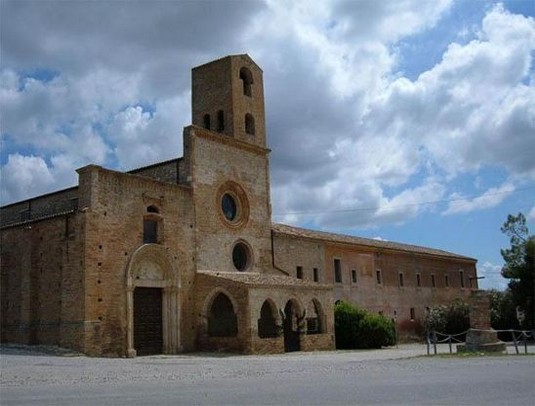 Abbazia di Santa Maria di Propezzano a Morro d’Oro (Te) Morro D'Oro conserva numerosi splendidi monumenti di varie epoche storiche, tra cui spiccano, nel centro del paese, la chiesa di S. Salvatore (1331), che custodisce una pregevole Madonna in terracotta policroma e alcune pitture su tela del seicento di Francesco Ragazzino. A qualche chilometro dal centro abitato il territorio di Morro D'Oro rifulge per la presenza della stupenda Abbazia di "S. Maria di Propezzano", fondata agli inizi dell'VIII secolo sotto Papa Gregorio II. La chiesa, uno dei Templi del cattolicesimo più belli ed antichi dell'intero Abruzzo, è Monumento Nazionale dal 1902. L'abbazia era molto apprezzata nel medioevo per la sua attività spirituale e diversi Pontefici la vollero premiare con la concessione di privilegi ed indulgenze. Chiesa di Santa Maria di Propezzano a Morro d'Oro: Il complesso conventuale di S. Maria di Propezzano (XIII / XIV sec.) sorge nel luogo dove la leggenda narra che sia apparsa la Madonna il 10 maggio del 715. Un enigma avvolge la costruzione della chiesa che, contrariamente alla successione storica degli stili: romanico, gotico, inspiegabilmente è stata iniziata in forme gotiche ed ultimata in forme romaniche. La facciata consta di tre parti di diversa altezza: le prime due concluse dal coronamento orizzontale, mentre la parte di destra è accorpata nel convento. Il corpo centrale ha un modesto corpo a tre archi ogivali appena accennati sotto il quale si apre il portale con gli antichi battenti e, intorno, resti di affreschi quattrocenteschi. Sopra il portico un oculo e, più in alto, un sobrio rosone. Il corpo di sinistra, d'altezza inferiore, ha un decorato portale detto "Porta Santa" che si apre solo il 10 maggio e il giorno dell'Ascensione. Appena arretrata rispetto alla facciata è la scarna Torre Campanaria quadrangolare. L'interno della Chiesa di Santa Maria di Propezzano a Morro d'Oro è a tre ampie navate divise da archi a tutto sesto e conserva resti di affreschi quattrocenteschi. Notevole è nell'attiguo convento il rustico Chiostro a pianta quadrata con doppio ordine di arcate a tutto sesto e pozzo nel mezzo; nelle lunette del Chiostro affreschi seicenteschi del pittore polacco Sebastiano Majescki. Nel refettorio affreschi cinquecenteschi di un ingenuo gusto popolaresco. Dove: Morro d'Oro Tipologia: Abbazia Periodo: secoli VIII-XIV. Fondazione e storia. L’abbazia, secondo la leggenda fondata nel 715, sorge nel comune di Morro d’Oro, nei pressi di Notaresco. Un’antica tradizione orale, poi riportata in una lunga iscrizione affrescata nel XV secolo sul prospetto della chiesa dal frate Andrea Cerone, racconta che la chiesa fu costruita a seguito di una divina richiesta: quando tre pellegrini tedeschi di ritorno dalla Terra Santa e in viaggio verso Roma sostarono in quella zona sotto un albero di Corniolo, la Vergine apparve loro in sogno mostrando il modello del tempio che desiderava fosse edificato in quel luogo. Fu così che i pii uomini costruirono la chiesa e la dedicarono a Maria; il pontefice Gregorio II appresa la notizia giunse da Roma, celebrò il rito e consacrò l’altare il 10 maggio del 715, donando alla chiesa importanti indulgenze. Tuttavia la trascrizione, pur rimanendo un importante documento, contiene alcune inesattezze, come il fatto che Gregorio II salì sul soglio pontificio solo il 19 maggio di quell’anno. Successivamente papa Bonifacio IX nel 1393 assegnò ulteriori privilegi e indulgenze alla chiesa di Chiesa di Santa Maria di Propezzano a Morro d'Oro e così fece anche il papa Martino V nel 1427, sperando di garantire una maggiore affluenza di fedeli alla chiesa. Alla fine del Quattrocento la famiglia degli Acquaviva d’Atri dominava il territorio circostante e giunse a impadronirsi anche di Propezzano, cosicché i suoi membri si alternarono alle cariche ecclesiastiche più importanti fino alla metà del Settecento. Seguì il patrocinio dei Pirelli fino a che all’inizio dell’Ottocento il marchese di Steirlich comprò il territorio comprensivo del convento. Oggi la chiesa appartiene alla diocesi di Teramo e alla parrocchia di Morrod’Oro. La facciata. A parte alcuni frammenti scultorei conservati all’interno della chiesa non rimane nulla dell’originaria costruzione del VIII secolo. L’abbazia, così come la vediamo oggi, risale alla seconda metà del Duecento e presenta gli elementi principali dell’architettura tardo romanica. Gli studiosi hanno trovato molte vicinanze stilistiche con il Duomo di Atri e con l’edilizia ecclesiastica borgognona. La ricostruzione avvenne in un momento di grande ricchezza e prestigio della zona e inaugura il ruolo di preminenza della chiesa rispetto al passato. Il prospetto, caratterizzato da uno sviluppo tendenzialmente orizzontale e rivestito di mattoncini in cotto, è molto articolato: alla facciata romanica è addossato un portico a tetto, mentre in corrispondenza della parte più bassa sulla destra si erge la torre campanaria, risalente al 1371. Le forme in generale sono semplici e severe, con poche concessioni decorative: il grande rosone superiore realizzato in cotto presenta più fasce concentriche con piccoli decori. Subito sotto un secondo rosone è stato aperto durante un recente restauro. Atri (Te). La cattedrale di Atri, eretta alla fine del Duecento sul luogo di una chiesa del IX sec. e, prima di questa, di un tempio della città romana Hatria, si affaccia sulla piazza di Atri. La splendida facciata, costruita in pietra di Bisenti, ha un imponente rosone a dodici raggi e un ricco portale eseguito da Rainaldo di Atri nei primi anni del trecento. Il lato destro è impreziosito da tre portali: il primo, di chiaro stile gotico, è di Rainaldo (1305); il secondo (1288) e il terzo (1302) sono di Raimondo del Poggio; tutti e tre hanno affreschi nelle lunette. Il campanile, alto più di 54 metri è stato ultimato alla fine del quattrocento da Antonio da Lodi con un tamburo ottagonale con bifore e ciotole maiolicate e rappresenta il prototipo dei campanili non solo teramani, ma anche abruzzesi. L’interno è a tre navate scandite da archi gotici; singolare è l’acquasantiera con donna rappresentata in costume tradizionale atriano. Il pavimento del presbiterio lascia intravedere, da lastre di cristallo, i mosaici di edificio termale romano. Ma il vero gioiello della chiesa sono gli affreschi del coro, ancora ben conservati, dipinti da Andrea de Litio (1450/1480) e che rappresentano il più grande ciclo pittorico del Rinascimento abruzzese. dipinti, diviso in tre fasce e composti da 101 pannelli, racconta le storie di Gesù e di Maria con una ricchezza di particolari attinti dal mondo quotidiano dell’artista. Notevole anche il chiostro duecentesco a tre ordini di arcate con al centro un raffinato pozzo decorato con volute nel 1763. Dal chiostro si scende nella Conserva d’acqua ricavata da una cisterna romana del II sec. d.C. che alimentava le terme; interessante il portale con rilievi del XI sec. e i cicli pittorici interni quattrocenteschi.