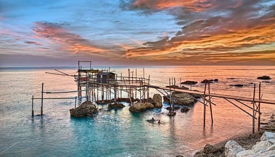 Il Trabocco nel chietino I trabocchi in Abruzzo hanno rappresentato per secoli un'importante risorsa per la pesca e la vita delle comunità costiere. La loro principale utilità era consentire ai pescatori di catturare il pesce senza dover affrontare i rischi del mare aperto, soprattutto in condizioni meteorologiche avverse. Grazie alla loro struttura stabile e ingegnosa, permettevano di pescare direttamente dalla riva, utilizzando un sistema di reti a bilanciere che venivano calate e sollevate manualmente con l'ausilio di argani. Oltre alla funzione primaria legata alla pesca, i trabocchi svolgevano un ruolo fondamentale anche come punto di riferimento e avvistamento lungo la costa. Posti su scogli o promontori, offrivano una visuale privilegiata sul mare, diventando simboli di controllo e sicurezza per le comunità locali. Alcuni trabocchi, più grandi e complessi, servivano persino come rifugio temporaneo o luogo di lavoro, unendo praticità e protezione per i pescatori. Nell’era moderna, i trabocchi hanno perso la loro funzione pratica per la pesca commerciale ma sono diventati un elemento centrale del patrimonio culturale e turistico dell’Abruzzo. Molti sono stati restaurati e trasformati in ristoranti, dove è possibile gustare piatti di pesce fresco immersi in un contesto unico e suggestivo. Questi locali offrono un'esperienza che valorizza la storia e la tradizione marinara, attirando visitatori da ogni parte del mondo. Infine, i trabocchi sono un simbolo dell’ingegno e dell’adattamento umano all'ambiente naturale. Rappresentano il legame tra uomo e mare, unendo passato e presente in una visione che sposa cultura, economia sostenibile e tutela del paesaggio costiero. Oggi, la loro utilità risiede nel preservare e promuovere l'identità abruzzese, rendendo la Costa dei Trabocchi un luogo iconico e di grande fascino.