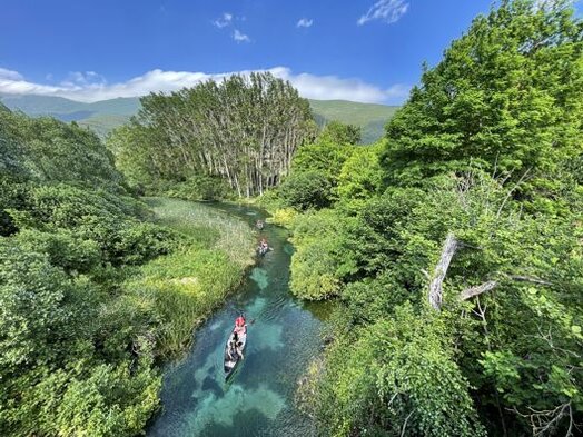 Trekking nelle valli dell’Abruzzo: La Valle del Tirino. Trekking nelle valli dell’Abruzzo: Valle del Tirino. La Valle del Tirino è un luogo dove la natura e la storia si intrecciano armoniosamente, regalando scenari di rara bellezza. Il fiume Tirino, con le sue acque limpide e dai riflessi turchesi, scorre tra colline rigogliose e antichi borghi, offrendo un’esperienza unica per chi desidera esplorarlo in canoa. I sentieri che attraversano la valle conducono tra distese di vigneti, boschi profumati e paesaggi mozzafiato, permettendo di scoprire un territorio autentico e incontaminato. Qui, ogni stagione regala colori e suggestioni diverse, rendendo ogni visita un’esperienza sempre nuova e affascinante. Percorrere i sentieri della Valle del Tirino significa immergersi nella sua storia millenaria, fatta di borghi abbandonati e antichi insediamenti che ancora raccontano il passato. L’itinerario parte dal Centro Turistico e Formativo Valle del Tirino e conduce verso San Silvestro, un borgo ormai disabitato ma ancora capace di evocare storie e tradizioni di un tempo. Proseguendo lungo il cammino, la vista si apre sui dolci declivi coltivati a vite, dove si producono alcuni dei migliori vini della regione, e si giunge fino alle sorgenti del fiume, nel suggestivo sito di Presciano, dove l’acqua cristallina sgorga tra rocce e vegetazione. Il percorso offre scorci panoramici di incredibile bellezza, con il borgo medievale di Capestrano che domina la valle e, sullo sfondo, le imponenti cime del Gran Sasso. Nelle giornate più limpide, l’orizzonte si apre fino a rivelare la vetta più alta dell’Appennino, il Corno Grande. Raggiunta la località di San Martino, una breve sosta permette di ammirare la trasparenza assoluta delle acque del Tirino, che qui riflettono il cielo con straordinaria nitidezza. Il cammino prosegue attraverso sentieri sterrati che si addentrano nella natura fino alla chiesa di San Pietro ad Oratorium, un prezioso esempio di architettura benedettina immerso nel verde. Prima di completare il percorso ad anello, vale la pena fermarsi su un punto panoramico da cui osservare dall’alto il fiume e la fauna che lo popola, regalando un momento di pace e contemplazione. Tornando verso San Martino, l’itinerario si conclude nei pressi della terza sorgente del Tirino, il Lago di Capodacqua, uno specchio d’acqua che conserva nel suo fondale i resti sommersi di antichi mulini. È qui che si chiude un viaggio tra natura, storia e tradizioni, lasciando nel cuore il ricordo di un angolo d’Abruzzo che incanta e sorprende a ogni passo.