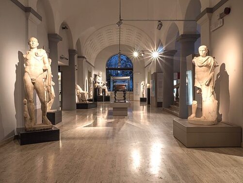 Musei e Raccolte in Abruzzo: Museo Archeologico Nazionale d'Abruzzo - Villa Frigerj a Chieti. Il Museo Archeologico Nazionale d'Abruzzo, ospitato nella suggestiva Villa Frigerj a Chieti, è un'importante istituzione culturale che custodisce il patrimonio storico e archeologico della regione. La villa, progettata dall'architetto Errico Riccio nel 1830 per volere del barone Ferrante Frigerj, sorge su una piccola altura che domina la città e offre una vista panoramica sulla villa comunale e sul massiccio montuoso della Majella. L'edificio, originariamente un terreno agricolo di proprietà della famiglia Frigerj, è stato trasformato in museo nel 1959 grazie all'interessamento dell’archeologo Valerio Cianfarani e, dal 2014, è entrato a far parte del Polo Museale dell'Abruzzo, diventando uno dei principali centri di ricerca e conservazione delle antiche civiltà che hanno abitato la regione. Il museo ospita una vasta collezione di reperti archeologici che vanno dalla protostoria fino all’alto Medioevo, con un percorso espositivo che racconta la storia delle antiche popolazioni abruzzesi. Tra i pezzi più rilevanti della collezione, spicca il celebre Guerriero di Capestrano, un capolavoro della statuaria preromana risalente al VI secolo a.C., che viene presentato in una sala dedicata, intitolata "Al di là del tempo". La curatela dell’allestimento di questa sezione è stata affidata all'artista Mimmo Palladino, che ha scelto di depurare il Guerriero dal suo significato storico per invogliare il pubblico a percepire il reperto in modo universale, al di là del suo contesto cronologico. Il piano terra del museo ospita anche una ricca sezione numismatica, che comprende una varietà di monete che documentano l’evoluzione delle civiltà che hanno abitato l’Abruzzo, e la collezione Pansa, che raccoglie oggetti eterogenei di epoca ottocentesca. Salendo al primo piano, il visitatore si immerge nella storia delle antiche popolazioni abruzzesi, tra cui i Vestini, i Peligni, i Marrucini e i Carricini, grazie ai reperti rinvenuti in importanti siti archeologici della regione. Gli oggetti esposti, provenienti da necropoli e santuari, permettono di comprendere le tradizioni, la vita quotidiana e le credenze di questi popoli, offrendo una visione approfondita della cultura materiale dell'Abruzzo antico. Il percorso museale prosegue con una sezione dedicata agli altri popoli dell’antico Abruzzo, come i Sabini, i Frentani, gli Equi e i Marsi. I manufatti esposti, che includono armi, utensili e altri oggetti di uso quotidiano, raccontano la storia di queste civiltà che hanno contribuito alla formazione del territorio abruzzese. Grazie alla bellezza architettonica della villa, la visita al Museo Archeologico Nazionale d'Abruzzo non è solo un'opportunità per esplorare il passato della regione, ma anche un’occasione per ammirare un edificio neoclassico che si integra perfettamente con la storia e le collezioni che ospita, creando un'esperienza culturale unica e affascinante.