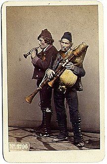 La fabbricazione di zampogne e strumenti musicali tradizionali in Abruzzo è un’arte che si tramanda di generazione in generazione, mantenendo viva una tradizione secolare che accompagna le festività e le celebrazioni religiose della regione. Gli artigiani abruzzesi che si dedicano a questa pratica sono esperti nel lavorare legni pregiati come l’ulivo e il ciliegio, materiali che conferiscono agli strumenti non solo una notevole resistenza, ma anche un suono caldo e naturale. Ogni strumento è realizzato a mano con un’attenzione meticolosa ai dettagli, dal taglio del legno alla lavorazione delle canne, affinché ogni zampogna produca il suono ricco e melodioso che la caratterizza. La cura del dettaglio è essenziale in ogni fase della fabbricazione. Dopo aver scelto il legno, gli artigiani lo modellano con grande precisione, prestando attenzione alle venature e alla consistenza del materiale, in modo che ogni strumento abbia una qualità unica. Il processo di lavorazione, che include la costruzione dei tubi e il trattamento delle canne per creare il suono, richiede grande esperienza. Ogni parte dello strumento viene scolpita e levigata con pazienza, per garantire che non solo l’estetica, ma anche la funzionalità sia impeccabile. Questo lavoro artigianale, che combina abilità manuale e conoscenza del legno, rende ogni zampogna un’opera d’arte a sé stante. Oltre alla zampogna, gli artigiani abruzzesi realizzano anche altri strumenti musicali tradizionali come tamburi e violini, che spesso accompagnano la musica folk locale. Questi strumenti sono utilizzati per celebrare eventi religiosi, festività popolari e tradizioni secolari che continuano a essere parte integrante della vita comunitaria. La realizzazione di ogni strumento non è solo un atto di produzione, ma anche un modo per mantenere viva la memoria storica e culturale della regione. Ogni suono che esce dalla zampogna o dal tamburo è un richiamo al passato, a una tradizione che unisce la musica alla spiritualità e alla festa. La tradizione della fabbricazione di zampogne e strumenti musicali in Abruzzo non è solo un processo che riguarda il passato, ma un’arte che vive nel presente e si adatta alle nuove esigenze. Oggi, molti artigiani continuano a lavorare questi strumenti per musicisti, collezionisti e appassionati, spesso realizzando strumenti su misura per eventi particolari. Sebbene il mercato musicale sia cambiato con l’avvento di strumenti moderni, la richiesta di strumenti tradizionali, realizzati a mano con metodi antichi, rimane viva. Questo perpetuare la tradizione garantisce che la cultura musicale abruzzese continui a essere apprezzata e valorizzata, sia a livello locale che internazionale.