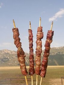 Gli arrosticini, uno dei piatti più amati della cucina abruzzese, rappresentano una tradizione culinaria radicata nella provincia di Teramo. Preparati con carne di agnello, questi spiedini sono simbolo di un territorio montano e selvaggio, dove l’agnello cresce al pascolo, nutrendosi delle erbe aromatiche che caratterizzano la flora locale. La carne viene tagliata a cubetti di dimensioni regolari e infilata su spiedini di legno o metallo, pronta per essere grigliata sulla brace. Il segreto di un buon arrosticino è la qualità della carne, scelta con cura per garantire morbidezza e sapore, tipici delle razze ovine presenti in Abruzzo, come la famosa "Pezzata rossa" o la "Sopravvissana". Il passo successivo nella preparazione degli arrosticini è la cottura sulla griglia, un momento cruciale che richiede pazienza e attenzione. Gli arrosticini vengono posti sulla brace viva, solitamente alimentata con legna di quercia o di altre piante locali, che conferisce un aroma inconfondibile alla carne. Durante la cottura, la carne viene spennellata con olio extravergine di oliva, uno degli ingredienti più preziosi dell'arte culinaria abruzzese. Questo olio, prodotto con olive della regione, esalta il sapore della carne e ne preserva la morbidezza, mentre la brace la sigilla all'esterno, creando una crosticina dorata. Aggiungere un rametto di rosmarino o, per chi lo preferisce, un pizzico di peperoncino, è una pratica comune per arricchire il sapore degli arrosticini. Il rosmarino, diffuso in tutta la regione, è un’erba aromatico che dona una fragranza particolare alla carne, unendo freschezza e intensità. Il peperoncino, che in Abruzzo è molto apprezzato, dona una leggera piccantezza che bilancia la delicatezza dell'agnello, conferendo ai piatti un tocco di vivacità. Questo piatto, che unisce la semplicità degli ingredienti e la maestria nella cottura, è un esempio perfetto di come i prodotti tipici abruzzesi possano trasformarsi in una delizia per il palato. Gli arrosticini vengono generalmente serviti caldi, accompagnati da un contorno di pane casereccio abbrustolito, spesso arricchito da un filo di olio extravergine d’oliva, per esaltare la croccantezza e la rusticità del piatto. Sebbene possano essere consumati come piatto principale, di solito vengono condivisi in convivialità, durante un pranzo all’aperto o in una festa tipica, dove la tradizione della grigliata è al centro della scena. L’arte degli arrosticini è una celebrazione della terra, delle sue tradizioni agricole e della passione abruzzese per il cibo genuino e preparato con amore.