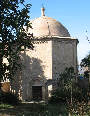 Tempietto del Tricalle. La chiesa di Sancta Maria a Tribus Callis sorge nell’omonimo quartiere del Tricalle, nel punto di innesto delle tre vie maestre (tribus callis) che collegavano la città di Chieti con la costa e con l’interno. La data della costruzione del Tempietto di Santa Maria del Tricalle non è certa; secondo Ferdinando Ughelli un’attestazione certa è riferibile al XIV secolo, quando era Vescovo di Chieti Pietro III, mentre il Bindi e il Nicolino ipotizzano datazioni più certe; il primo richiama un’edificazione del 1317 sulle fondamenta di un tempio dedicato a Diana Trivia, mentre il secondo, nella sua “Historia della città di Chieti”, in base ad un’iscrizione oggi scomparsa la vuole costruita nel 1322. È del 1939 un’interessante pubblicazione di un quotidiano locale che riporta l’articolo approfondito del prof. Francesco Verlengia, che non accetta letteralmente tali ipotesi, poiché non proprio la morfologia ottagona del monumento, che è di certo riferibile ai battisteri di epoca romana, quanto più l’elevato, ricorda più letteralmente l’architettura lombarda quattrocentesca. In effetti, secondo il Verlengia, il laterizio a vista, le decorazioni geometriche, gli archetti ad ogiva e la cupola sormontata da un torrino cilindrico ricordano molto il rinascimento lombardo, tanto da far pensare ad un parallelismo tra il Tempietto e la cupola del campanile della Cattedrale teatina. Il progetto della torre campanaria di San Giustino infatti porta la firma dell’architetto lombardo Antonio da Lodi, che nel 1498 concluse la costruzione dell’ultimo livello; dello stesso autore sono anche il campanile della Basilica di Santa Maria Assunta di Atri, del campanile del Duomo di Teramo, della Chiesa di Santa Maria in Platea di Campli e della parrocchiale di Sant’Agnese di Corropoli. Secondo altre ipotesi l’aspetto decorativo più nordico del monumento risale ad un rinnovamento quattrocentesco dell’impianto originale, in particolare proprio il coronamento e la cupola. Il Tempietto del Tricalle conserva la sua morfologia armonica, compresa di un ampio portico, fino ai lavori del 1879, quando un restauro troppo ardito portò alla demolizione dell’annesso, lasciando il tempio ottagono completamento libero su tutti i prospetti. In una nota dell’11 agosto del 1894 trasmessa dal Ministero della Pubblica Istruzione – Divisione per i monumenti e le scuole d’arte alla Direzione Regionale per la conservazione dei monumenti è possibile raccogliere informazioni di cantiere relativi proprio ai restauri del 79. Dalla lettera a firma del Ministro si legge che il progetto originale prevedeva una spesa di 1324.53 Lire, aumentate a 2775.44 Lire a seguito del deposito presso il competente ufficio del Genio Civile provinciale; i lavori riguardavano il consolidamento dell’estradosso della cupola con rinforzo in calcestruzzo. Ma nella nota si legge anche che “al momento di metter mano all’opera, sorse il dubbio se dovessero i restauri estendersi anche ad una cappellina aggiunta al tempietto in epoca molto posteriore alla costruzione di esso, o se non convenisse invece demolirla. La locale Commissione conservazione dei monumenti, affermando che quella fabbrica contrastava con il carattere e lo stile del tempio, opinò che potesse togliersi, e così fu fatto”. Se il riferimento alla cappellina fosse da intendersi rispetto al portico o rispetto ad una superfetazione questo non è chiaro, ma la certezza è che a seguito dei lavori del ’79 dell’antico ampio portico resta solo una piccola porzione ruderizzata nell’angolo sinistro della scalinata di accesso. Riguardo il rapporto tra il monumento e il suo contesto, la sua localizzazione che la collocava in eccellente posizione soprelevata rispetto alle vie di accesso alla città è divenuta nel tempo una forte fragilità. Nel 1908, con la costruzione della ferrovia elettrica che la costeggiava, i riempimenti di terreno e la riorganizzazione urbanistica della zona del Tricalle finirono per rialzare la quota di attestazione del nuovo assetto, tanto da relegare il tempietto ad una quota di oltre due metri al di sotto del piano stradale. Evidentemente tale operazione fu supportata dallo stato di abbandono del monumento, non più officiata già dal XIX secolo, la cui funzione passò da chiesa cimiteriale a magazzino comunale. Nella metà del Novecento fu finalmente riportata alla luce, con operazioni di restauro e di pulizia e soprattutto di valorizzazione dello spazio esterno, con la piantumazione dei cipressi e la sistemazione dell’accesso. Negli ultimi anni del secolo scorso fu nuovamente restaurata dalla Soprintendenza Belle Arti e Paesaggio dell’Abruzzo. Oggi il Tempietto, di proprietà del Demanio dello Stato, anche grazie a piccole operazioni di restyling, di adeguamento impiantistico e dell’accessibilità è un luogo culturale, uno spazio che viene restituito alla città. L’edificio monumentale si presenta oggi con dimensioni contenute e proporzionate, con uno spazio interno di circa 90 metri quadri. La pianta è ottagona, con quattro piccole esedre poste nei prospetti interni verso l’ingresso. L’interno della chiesa è uno spazio pulito, semplice e slanciato, ricoperto di intonaco bianco, certamente non originale. Si leggono nello spazio bianco i 4 archetti in laterizio delle esedre laterali e dell’arco di fondo, nonché la cornice di coronamento e i costoloni della volta ottagonale. Dalla porticina di destra si accede ad una strettissima gradinata ricavata nello spessore murario che conduce ad una delle finestrelle, dalla quale è possibile leggere dall’alto l’impianto geometrico del monumento. All’interno e all’esterno del Tempietto sono stati eseguiti in passato piccoli scavi, dai quali sono emerse tombe e risultanze delle attestazioni murarie dell’antico edificio.