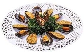La preparazione delle cozze al gratin nella tradizione della provincia di Teramo è un perfetto esempio di come i sapori autentici del mare possano fondersi con i prodotti tipici abruzzesi per creare un piatto dal gusto unico. Le cozze, fresche e saporite, vengono accuratamente pulite per eliminare ogni impurità, mantenendo intatta la loro essenza marina. La pulizia, che comprende la rimozione del bisso e delle incrostazioni, è un passaggio fondamentale per garantire la qualità del piatto, che si basa sull’integrità e sulla freschezza degli ingredienti. Un elemento chiave della ricetta è la panure, preparata con pangrattato, prezzemolo fresco e aglio, a cui si aggiungono i capperi tritati per un tocco di sapidità. Il pangrattato, spesso fatto in casa utilizzando pane locale abruzzese, dona alla gratinatura una consistenza croccante e un sapore autentico. L’olio extravergine di oliva, proveniente dagli uliveti abruzzesi, arricchisce la farcitura con il suo aroma fruttato, esaltando ogni singolo ingrediente. Per completare, un pizzico di sale e pepe, dosati con cura, conferisce equilibrio e carattere alla preparazione. Una volta farcite con il composto, le cozze vengono adagiate su una teglia rivestita con carta forno. Prima di infornare, il tocco distintivo arriva dall’aggiunta di un po’ del liquido di cottura delle cozze, filtrato per eliminare eventuali residui. Questo ingrediente, ricco di sapore, lega il ripieno e intensifica il profumo del mare, che si sprigiona durante la cottura. In forno, a temperatura elevata, le cozze sviluppano una crosta dorata e croccante, mentre l’interno rimane morbido e succulento, offrendo un contrasto irresistibile. Il risultato finale è un antipasto che celebra il connubio tra i sapori del mare e i prodotti della terra abruzzese. Le cozze al gratin, servite calde direttamente dal guscio, sono perfette per essere accompagnate da un bicchiere di Trebbiano d’Abruzzo, il vino bianco locale che completa armoniosamente il piatto. Questa ricetta, espressione della tradizione teramana, racchiude l’essenza di una cucina che valorizza la semplicità degli ingredienti e il piacere della convivialità.