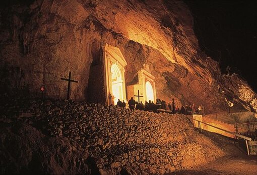 Le Grotte naturali in Abruzzo: Grotta Rupestre e Santuario di Sant'Angelo - Balsorano (Aq). La Grotta Rupestre e il Santuario di Sant'Angelo, situati nei pressi del paese di Balsorano, rappresentano uno dei luoghi più suggestivi e spiritualmente significativi dell'Abruzzo. Percorrendo un sentiero lastricato che si snoda tra la natura montuosa, si giunge a una piccola grotta dedicata a Sant'Angelo, il cui fascino è accentuato dalla storia antica che la circonda. Questo luogo di culto, che risale probabilmente all’epoca romana, è stato per secoli un rifugio per eremiti e pellegrini, e conserva ancora oggi un'atmosfera di quiete e sacralità, immersa nel cuore del Parco Regionale dei Monti Simbruini. Sulla destra dell'ingresso della grotta si possono osservare i resti di un antico monastero benedettino, di cui rimangono solo scarse tracce murarie. A poca distanza dalla grotta, un edificio più recente, costruito tra il 1750 e il 1800 grazie alle donazioni dei fedeli, ha sostituito le modeste abitazioni degli eremiti, includendo refettori, cucine e camerate. Questo nuovo complesso, che si sviluppa su due piani superiori, divenne il cuore delle attività religiose locali, ospitando pellegrini e monaci in cerca di un luogo di ritiro e meditazione. L’ingresso della grotta è protetto da un muretto basso e da un'inferriata, mentre due edicole e un piccolo pozzo arricchiscono il paesaggio sacro che circonda il sito. Nel cuore della grotta si trova una zona cultuale profonda circa 20 metri, percorsa da un ampio gradone centrale che collega i vari altari dedicati ai santi. I due altari principali, dedicati a San Michele Arcangelo e al Santo Spirito, sono accessibili tramite due scalinate e sono adornati con dipinti di grande valore. Altri altari, dedicati a San Giuseppe e a Sant'Antonio da Padova, sono situati più in basso, mentre l'altare della Madonna Addolorata è custodito in una piccola cappella a destra dell’ingresso. Ogni angolo della grotta è impregnato di spiritualità, e la sua atmosfera raccogliente invita alla preghiera e alla riflessione profonda. La storia della Grotta Rupestre è legata a una leggenda che narra di un uomo di nome Angelo, un vassallo del barone di Balsorano, che, dopo aver scoperto il tradimento del suo padrone con sua moglie, si rifugiò sui monti, dando inizio a una dura persecuzione nei confronti del barone. La sua vicenda culminò con l'incidente del figlio del nobile, che fu salvato da un misterioso individuo, poi identificato come Angelo stesso. Da quel momento, Angelo condusse una vita eremitica nella grotta, dove morì alcuni anni dopo. Il monastero fu fondato ufficialmente nel 1273, e il culto di Sant'Angelo divenne sempre più radicato, con la celebrazione di esercizi spirituali che si svolgono ancora oggi, attirando pellegrini nei mesi di maggio e settembre. Questo luogo, intriso di fede e leggende, continua a essere un punto di riferimento per chi cerca la pace interiore e il contatto con la natura e la spiritualità.