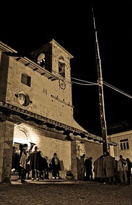 A Tornimparte, ogni anno, la notte tra il 30 aprile e il 1° maggio si celebra un’antica tradizione chiamata "Ju Calenne", che ha radici profonde nella cultura popolare del paese. Questo rito, noto anche come l'Albero del Maggio, si svolge in un'atmosfera carica di fascino e sacralità. Un gruppo di uomini, rigorosamente selezionato, si reca nei boschi vicini al paese per tagliare un albero maestoso, alto e diritto, che dovrà essere portato davanti alla chiesa del Santo Patrono prima dell’alba. L'albero, simbolo di rinascita e fertilità, resterà fissato davanti alla chiesa fino alla fine del mese di maggio, per poi essere abbattuto e venduto in un'asta pubblica. Questa tradizione, che unisce il sacro e il profano, si svolge ogni anno con un’intensità che mantiene viva la memoria di un passato lontano. Le origini di "Ju Calenne" si intrecciano con la storia dei Longobardi, un popolo che, come testimoniato dai toponimi di origine germanica presenti nel territorio, aveva una forte connessione con la natura e il culto degli alberi. L'Albero del Maggio, infatti, affonda le sue radici in rituali antichi che celebravano la primavera e la fertilità della terra, temi centrali nelle tradizioni pagane. La scelta di un albero maestoso da erigere simbolicamente davanti alla chiesa riflette il legame profondo tra l’uomo e la natura, un legame che si perpetua da secoli. Sebbene oggi il rito abbia perso gran parte del suo significato pagano, rimane un simbolo di forza, speranza e rinnovamento per la comunità di Tornimparte. Il paesaggio naturale di Tornimparte, ricco di boschi e foreste, offre lo scenario ideale per questa festa. Le alte montagne, dominati da faggi e altre piante tipiche dell'Appennino, sono parte integrante di questa tradizione. I boschi non erano solo una risorsa economica per la comunità, ma anche un luogo sacro, un rifugio per i miti e le leggende che si tramandano di generazione in generazione. Fino agli anni ‘50, il legame con la terra era talmente profondo che l’intera economia del paese dipendeva dal bosco e dalle sue risorse. Questo legame si traduceva in pratiche come il taglio ceduo, un metodo di gestione forestale che permetteva alla natura di rigenerarsi e che garantiva alla comunità risorse vitali come legna, foraggio e carbone. La festa del 1° maggio a Tornimparte non si limita però al solo rito dell'Albero del Maggio. Si intreccia con altre tradizioni locali, come la festa di San Panfilo, il patrono di Villagrande, una frazione del comune. La benedizione delle sementi, la scelta dei pastori e il ramo di faggio fiorito, simbolo della fine dell’inverno e del ritorno della vita, sono segnali di un'epoca in cui l'agricoltura e la pastorizia erano l’anima della comunità. Ogni gesto, ogni rito, aveva un significato profondo legato al ciclo della natura e alla sopravvivenza. Il ramo di faggio, esposto davanti alla chiesa, rappresentava il segno di speranza per la fine dei rigori invernali e l'inizio della stagione della crescita. Oggi, seppur con le inevitabili trasformazioni portate dalla modernità, "Ju Calenne" rimane una delle tradizioni più sentite dalla comunità. Sebbene la festa non abbia più il carattere sacro e magico di un tempo, continua a rappresentare un momento di unione e di celebrazione collettiva. I giovani partecipano con entusiasmo, imparando dagli anziani come si erige l'albero e riscoprendo l’importanza della tradizione. Ogni anno, la notte del 30 aprile si trasforma in un’occasione unica per vivere un’esperienza che unisce passato e presente, per mantenere viva la memoria storica e culturale di Tornimparte, un paese che custodisce gelosamente le sue radici e la sua identità.
