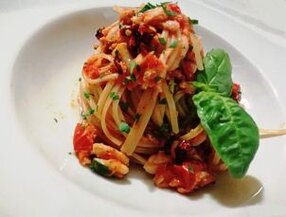 La cucina della provincia di Teramo è ricca di sapori autentici e tradizioni marinare, come dimostrano le Linguine di pappagallo al sugo di razza alla giuliese. Questo primo piatto è un omaggio al mare e alla semplicità degli ingredienti, un equilibrio perfetto tra genuinità e gusto. La ricetta, pensata per sei persone, richiede pochi ingredienti: una razza di circa 750 grammi (o più razze piccole, per semplificare la preparazione), 600 grammi di linguine di pappagallo, 500 grammi di pomodori pelati, due spicchi d'aglio, un mazzetto di prezzemolo fresco e sei cucchiai di olio extravergine d’oliva. Il procedimento inizia con la pulizia della razza. Nel caso di un esemplare grande, è necessario spellarla, pulirla accuratamente e tagliarla in pezzi, mentre per razze più piccole si può saltare questa operazione. In una padella capiente, scaldate l’olio e fate rosolare l’aglio intero, aggiungendo poi i pomodori pelati e il prezzemolo tritato. Lasciate cuocere a fiamma dolce per circa dieci minuti, mescolando di tanto in tanto, affinché il sugo si insaporisca. Aggiungete quindi i pezzi di razza, lasciando che il pesce si integri al condimento. Nel frattempo, portate a ebollizione una pentola con abbondante acqua salata e cuocete le linguine di pappagallo fino a raggiungere una consistenza al dente. Questa tipologia di pasta, tipica della zona, è perfetta per raccogliere il sapore del sugo. Una volta pronte, scolate le linguine e trasferitele direttamente nella padella con il sugo di razza. Saltate il tutto a fiamma vivace per qualche minuto, in modo che il condimento si amalgami perfettamente alla pasta, esaltandone il sapore. Servite le Linguine di pappagallo al sugo di razza ben calde, guarnendo i piatti con una spolverata di prezzemolo fresco per un tocco di colore e freschezza. Questo piatto rappresenta una celebrazione del mare e della cucina teramana, capace di esaltare ingredienti semplici con tecniche tradizionali. Le varianti locali, come l’utilizzo di razze piccole, testimoniano la versatilità e l’ingegnosità di una gastronomia che si adatta alle risorse disponibili senza mai perdere il suo fascino unico.