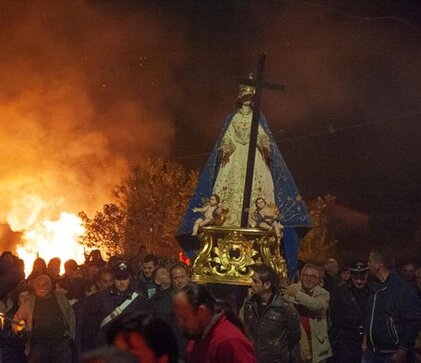 La Festa della Madonna della Croce a Pietranico è una delle celebrazioni più sentite e radicate nella tradizione popolare abruzzese, che si svolge ogni anno il 2 maggio. La festa ha origine nel lontano 1675 e affonda le sue radici in un atto di devozione popolare che ha segnato la vita del paese. Secondo la tradizione, la Madonna della Croce ha protetto Pietranico dalle scorrerie dei briganti, e ogni anno i fedeli partecipano alla processione in segno di gratitudine e di preghiera. Al tramonto del 2 maggio, la statua della Madonna viene portata in processione dalla chiesa parrocchiale di San Michele e Santa Giusta per le vie del centro storico, seguita da una folla devota che, con torce e rosari in mano, accompagna il cammino della Vergine. La tradizione della processione è accompagnata da un evento particolarmente suggestivo: lungo il percorso vengono accese delle cataste di ginestre che, con il loro crepitio e le alte fiamme, creano un’atmosfera che avvolge l’intero paese. Il fuoco, che rappresenta simbolicamente la purificazione e la protezione, ha origini antichissime legate ai culti solari. Questo rito richiama antiche tradizioni, come quelle celtiche, che segnavano i mutamenti stagionali e il ciclo agricolo. Sebbene oggi il fuoco abbia principalmente un significato religioso, una volta aveva anche una funzione propiziatoria per l’agricoltura e la transumanza, tradizione che era molto radicata a Pietranico, situato lungo il Tratturo Magno. Il fuoco, infatti, rappresentava per i pastori un simbolo di protezione, soprattutto durante il passaggio delle greggi dalle montagne abruzzesi verso la pianura pugliese. Pietranico, grazie alla sua posizione strategica lungo il Tratturo Magno, era un importante punto di sosta per i pastori e le loro greggi. Oggi, questa connessione con la vita rurale e pastorale viene ricordata attraverso il fuoco e il suo legame con la terra e la transumanza, ma anche con la protezione divina della Madonna. Un altro elemento distintivo della festa è il culto delle Sette Madonne Sorelle, un aspetto devozionale mariano che lega Pietranico a diverse chiese sparse nella regione. Ogni anno, i fedeli si recano a piedi a visitare questi santuari, tra cui l’Oratorio di Santa Maria della Croce, situato a due chilometri dal paese. Questo luogo sacro è legato a una tradizione che affonda le sue radici in un'apparizione della Madonna avvenuta nel 1613. La statua della Madonna della Croce viene portata all’Oratorio il 3 maggio, per poi ritornare nel pomeriggio nella chiesa parrocchiale. Questa parte del pellegrinaggio, un tempo fatta a piedi, è oggi diventata un viaggio in camioncino, segno dei cambiamenti nelle tradizioni nel corso degli anni. Nonostante il mutamento nelle modalità di celebrazione, la Festa della Madonna della Croce continua a rappresentare un momento di forte identità per la comunità di Pietranico. Le tradizioni che la accompagnano, come la processione con le torce, il fuoco e la preghiera, sono ancora oggi un'occasione di unione per la popolazione locale, che vive la festa con devozione e partecipazione. Sebbene alcuni aspetti della tradizione siano cambiati nel tempo, la forza spirituale e comunitaria di questo evento continua a rendere la festa un punto di riferimento importante nella cultura e nella religiosità popolare della provincia di Pescara.