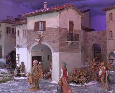 Presepe artistico a Pescara (Pe). A Pescara, durante il periodo natalizio, la tradizione dei presepi artistici assume un ruolo di grande importanza culturale, tanto da attrarre ogni anno visitatori da ogni angolo d'Italia. Le mostre dedicate a queste creazioni artigianali si svolgono in vari luoghi significativi della città, e rappresentano un’occasione per celebrare il Natale attraverso un’arte che unisce la fede, la tradizione e la creatività. I presepi esposti sono realizzati con materiali diversi e inusuali, tra cui sughero, argilla, terracotta, pietra bianca della Maiella, polistilene e persino bossoli di proiettile, che conferiscono a ogni opera un carattere unico e originale. Le creazioni non si limitano alla sola rappresentazione della Natività, ma spesso ricreano interi villaggi, paesaggi montani e scene di vita quotidiana, mettendo in risalto l’ingegno e la maestria degli artigiani. Uno degli appuntamenti più rilevanti di questa tradizione è la Mostra nazionale del presepe artistico, allestita nei locali parrocchiali della chiesa di Sant’Antonio di Padova. La mostra, curata dalla sede di Penne dell’Associazione italiana amici del presepe artistico, è un viaggio tra le opere di 22 artisti italiani che si distinguono per l’eccellenza delle loro creazioni. Queste sculture non si limitano alla rappresentazione statica della scena della Natività, ma raccontano storie più ampie, grazie all’inserimento di dettagli scenografici che catturano l'osservatore. Ogni pezzo sembra raccontare una storia attraverso le luci, le ombre, le prospettive e la disposizione dei personaggi, che interagiscono tra loro in un gioco di vita quotidiana e spiritualità. Un altro luogo di grande importanza per la tradizione dei presepi a Pescara è il Circolo Aternino, dove è allestita una mostra che ospita oltre cento presepi, molti dei quali provenienti dalla tradizione abruzzese e napoletana. Questi presepi, realizzati con materiali come il sughero, la terracotta e la pietra bianca della Maiella, rappresentano non solo la Natività, ma anche la cultura e la storia del territorio. L’esposizione è anche un’occasione di solidarietà: le offerte raccolte durante la visita vengono infatti destinate a un fondo per l’acquisto di attrezzature per il reparto epatico dell’Ospedale di Penne, un gesto che unisce l’arte alla generosità. La bellezza delle opere esposte diventa quindi un mezzo per sostenere cause nobili, rendendo la mostra ancora più significativa per la comunità. Inoltre, la tradizione dei presepi artistici a Pescara si arricchisce con eventi speciali che coinvolgono tutta la cittadinanza. Tra questi, la rappresentazione del corteo dei Magi, che ogni anno viene messa in scena il 6 gennaio, giorno dell’Epifania. Questo evento, che rievoca l’antica tradizione dei Magi che portano i doni al Bambino Gesù, è un momento di grande partecipazione popolare. I bambini e le famiglie si ritrovano per assistere a una performance che, tra luci e musiche, racconta un capitolo della storia cristiana con un tocco di teatralità che arricchisce ulteriormente il significato della festa. La presenza della Befana, che distribuisce calze ai più piccoli, aggiunge un elemento di allegria e spensieratezza, rendendo la giornata un’occasione di gioia per tutta la comunità. Infine, un’altra esposizione di particolare interesse è quella organizzata dall’associazione Mousiké, che presenta una collezione di 600 presepi provenienti da 88 paesi del mondo. Tra le opere più originali ci sono quelle realizzate con materiali inusuali, come i gusci di pistacchio o i bossoli di proiettile provenienti da conflitti lontani. Queste opere, così come il presepe napoletano in stile tradizionale, con i personaggi vestiti nei costumi tipici di ogni paese d’Abruzzo, raccontano come l’arte del presepe si sia diffusa e adattata alle diverse culture. La mostra di Mousiké, quindi, non è solo un’esposizione di bellezza, ma anche un punto di incontro tra tradizione, innovazione e interculturalità, che offre a chi la visita un'esperienza unica e arricchente, facendo della città di Pescara un centro di richiamo per gli appassionati di arte e folklore natalizio.
