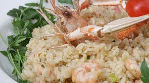 Il risotto sogliola e scampi, un piatto tipico della cucina abruzzese, comincia con la preparazione di un brodo ricco, che sarà la base di tutto il piatto. Per il brodo, si utilizzano scarti di scampi e gamberi, ingredienti pregiati che provengono dalle acque del mare Adriatico, nelle vicinanze della provincia di Teramo. Questi scarti vengono uniti a verdure fresche come carote, sedano e cipolla, che donano al brodo un sapore delicato ma aromatico. L’acqua bollente, con l'aggiunta di un po' di sale, permette di estrarre tutto il gusto del mare e delle verdure, creando un fondo perfetto per il risotto. Per la preparazione del risotto, si inizia facendo soffriggere aglio, cipolla e peperoncino, che sono aromi tipici della cucina abruzzese, in un paio di cucchiai di olio extravergine di oliva, prodotto con olive locali e molto usato in ogni piatto della tradizione regionale. Una volta che il soffritto è ben dorato, si aggiungono i gamberi e gli scampi precedentemente puliti, facendo cuocere brevemente, fino a che non rilasciano i loro succhi. A questo punto si unisce il riso, che viene tostato nel soffritto, un passaggio fondamentale per esaltare i sapori e renderlo più profumato. Quando il riso è ben tostato, si sfuma con un po' di Brandy, un altro ingrediente che si ritrova nella cucina teramana in alcune ricette, e si comincia ad aggiungere il brodo di pesce preparato in precedenza. Durante la cottura del riso, il brodo viene versato poco alla volta, in modo che il riso assorba gradualmente i suoi sapori. Il brodo arricchisce ogni chicco di riso con il gusto del mare, mentre il pepe e il prezzemolo fresco tritato, che sono ingredienti comuni nella cucina abruzzese, donano un tocco di freschezza e aromaticità al piatto. Nel momento in cui il risotto è quasi pronto, si aggiungono i filetti di sogliola, che conferiscono al piatto una morbidezza unica, accompagnata dalla dolcezza degli scampi e dei gamberi. Dopo aver mantecato il risotto, si completa il piatto con la decorazione degli scampi interi, lasciati da parte in precedenza. Questo risotto, ricco di sapori marini e arricchito da prelibatezze abruzzesi, è un piatto che porta in tavola tutta l’autenticità e la freschezza della cucina teramana, combinando ingredienti semplici ma di qualità in una preparazione raffinata.