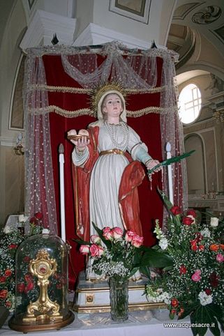 Il 5 febbraio di ogni anno, il piccolo comune di Civitaluparella, nel cuore della provincia di Chieti, celebra con grande devozione la festa in onore di Sant'Agata, una delle ricorrenze religiose più sentite nella zona. Questa data, che ricorda il martirio della Santa avvenuto nel 251 d.C. sotto l'imperatore Decio, è profondamente radicata nella tradizione locale. La storia di Sant'Agata, giovane donna di nobili origini che rifiutò la proposta di matrimonio del console Quinziano, è segnata dalla sua fermezza nella fede cristiana e dalla tragica violenza con cui fu punita. Il suo martirio, che include torture fisiche, viene commemorato simbolicamente in numerosi riti, tra cui la tradizionale benedizione del pane, che ricorda il dolore inflitto alla santa durante la sua agonia. A Civitaluparella, la festa non è solo un momento di preghiera, ma una celebrazione che unisce l’intera comunità attraverso il folklore e la partecipazione attiva. Il cuore della festa è rappresentato dalla solenne messa e dalla processione, che vedono i fedeli percorrere le strade del paese in onore della Santa. Tuttavia, l’aspetto più distintivo di questa tradizione popolare è la sfilata delle “conocchie”, che costituiscono una manifestazione di grande valore simbolico. Le donne del paese, vestite nei tradizionali costumi popolari, portano donativi alimentari che vengono offerti durante la processione, come gesto di gratitudine e di devozione verso la Santa. Questo rito richiama simili tradizioni presenti in altre località abruzzesi, ma assume un significato particolarmente forte a Civitaluparella, dove la comunità si ritrova unita in un gesto collettivo di fede. Civitaluparella è un luogo che, oltre alla sua bellezza naturale, riesce a evocare una profonda sensazione di appartenenza, soprattutto durante le celebrazioni di Sant'Agata. Il paese, arroccato su un colle che offre una vista spettacolare sulla vallata del Sangro e sulle maestose montagne circostanti, è il palcoscenico perfetto per una festa che affonda le sue radici nella storia e nella cultura abruzzese. Il centro storico, con le sue stradine strette e le antiche case in pietra, si anima di colori, suoni e preghiere, creando un’atmosfera unica che coinvolge tutti i partecipanti, dai più anziani ai bambini, in un atto di memoria e devozione che si tramanda da generazioni. La Chiesa di San Pietro Apostolo, cuore spirituale di Civitaluparella, ospita l’altare maggiore con la statua di Sant'Agata, ed è il luogo dove si celebrano le principali funzioni religiose della festa. Questa chiesa, che un tempo era una Badia Benedettina, si distingue per la sua struttura a due navate e la copertura a cupola nelle cappelle laterali. Oltre alla messa, durante la festa viene celebrato il culto di Sant'Agata con una particolare attenzione al simbolismo legato al suo martirio. L'altare dedicato alla Santa è adornato con fiori e candele, mentre le statue di altri santi, come San Rocco, sono presenti nella navata laterale, arricchendo l’atmosfera di sacralità che pervade tutto il paese. Nonostante il trascorrere degli anni, la festa di Sant'Agata a Civitaluparella mantiene viva una tradizione che lega la comunità al suo passato, ma che al contempo si rinnova ogni anno. La partecipazione alla processione e alla sfilata delle conocchie, insieme alla forte identità religiosa e culturale, fanno di questa festa un momento fondamentale per la vita del paese. Seppur meno celebrata rispetto al passato, la festa continua a rappresentare un’occasione di incontro e di riflessione spirituale per i civitani e per i numerosi pellegrini che giungono da altri paesi dell’Abruzzo. In questo contesto, Civitaluparella si conferma come uno dei luoghi più significativi per la conservazione delle tradizioni religiose e popolari della provincia di Chieti.