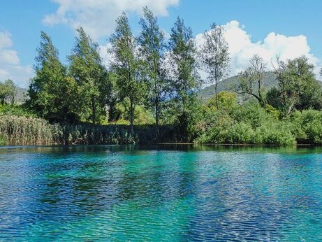 Nel cuore dell’Abruzzo, alle pendici del massiccio del Gran Sasso, si trova la Riserva Naturale Regionale “Le Sorgenti del Pescara”, un’area protetta di straordinario valore ambientale situata nel territorio di Popoli, in provincia di Pescara. Questa riserva, istituita nel 1986, tutela uno dei più importanti sistemi sorgentizi dell’Italia centrale: le acque limpide che sgorgano a valle alimentano il fiume Pescara e danno origine a un ambiente ricco di biodiversità. Il paesaggio è dominato da canneti, stagni, piccoli ruscelli e una vegetazione lussureggiante che ospita una fauna variegata, rendendo l’area un habitat ideale per numerose specie acquatiche e di uccelli migratori. Grazie alla presenza costante dell’acqua e all’integrità degli ecosistemi, la riserva rappresenta un importante laboratorio naturale. Qui si svolgono attività di ricerca scientifica, monitoraggio ambientale ed educazione ecologica, coinvolgendo scuole, enti e visitatori. Il centro visite, situato all’interno della riserva, propone percorsi didattici e iniziative volte a far conoscere il fragile equilibrio che regola le zone umide e a promuovere una cultura della sostenibilità. Le Sorgenti del Pescara sono anche un esempio virtuoso di come la protezione dell’ambiente possa integrarsi con l’esperienza turistica e la valorizzazione del territorio. Visitare la riserva significa immergersi in un ambiente incontaminato, dove il tempo sembra rallentare e ogni elemento naturale rivela la sua importanza. I sentieri che costeggiano le acque sorgive offrono un’esperienza sensoriale unica, tra suoni d’acqua, riflessi di luce e il volo improvviso di un airone. Questo angolo verde d’Abruzzo, facilmente accessibile ma al tempo stesso straordinariamente protetto, è un invito a riscoprire il valore della natura e a partecipare alla sua tutela attiva.